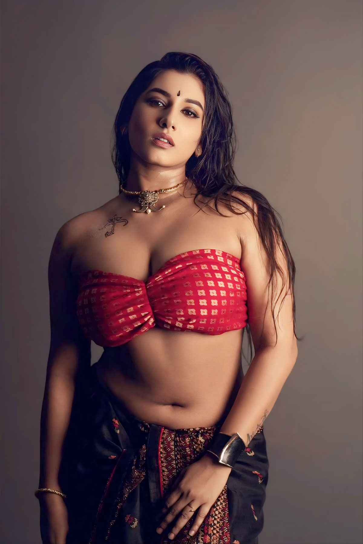 Vishnupriya, a curvy Indian woman in a red patterned bandeau tube top and black skirt with a chest tattoo.