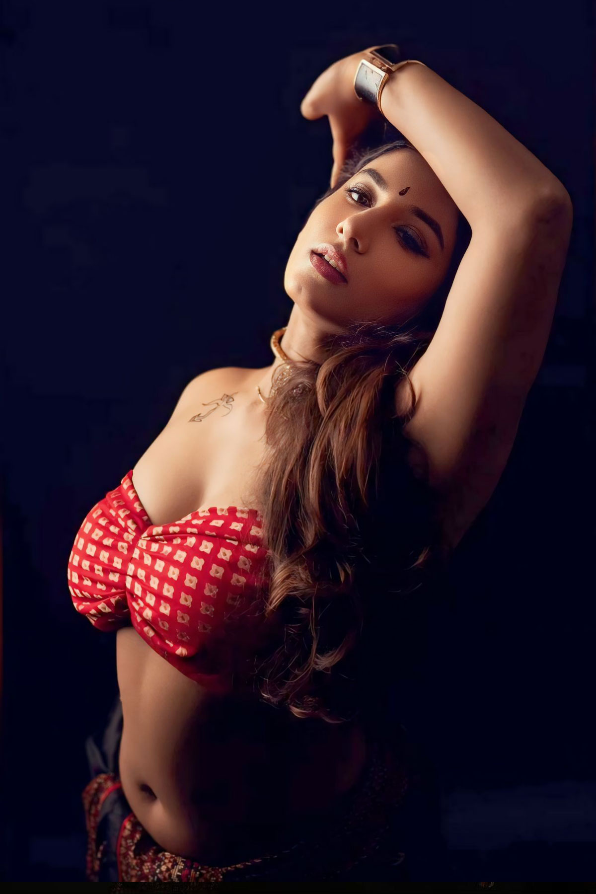 Vishnupriya, a curvy Indian woman in a red patterned bandeau tube top and black skirt with a chest tattoo.