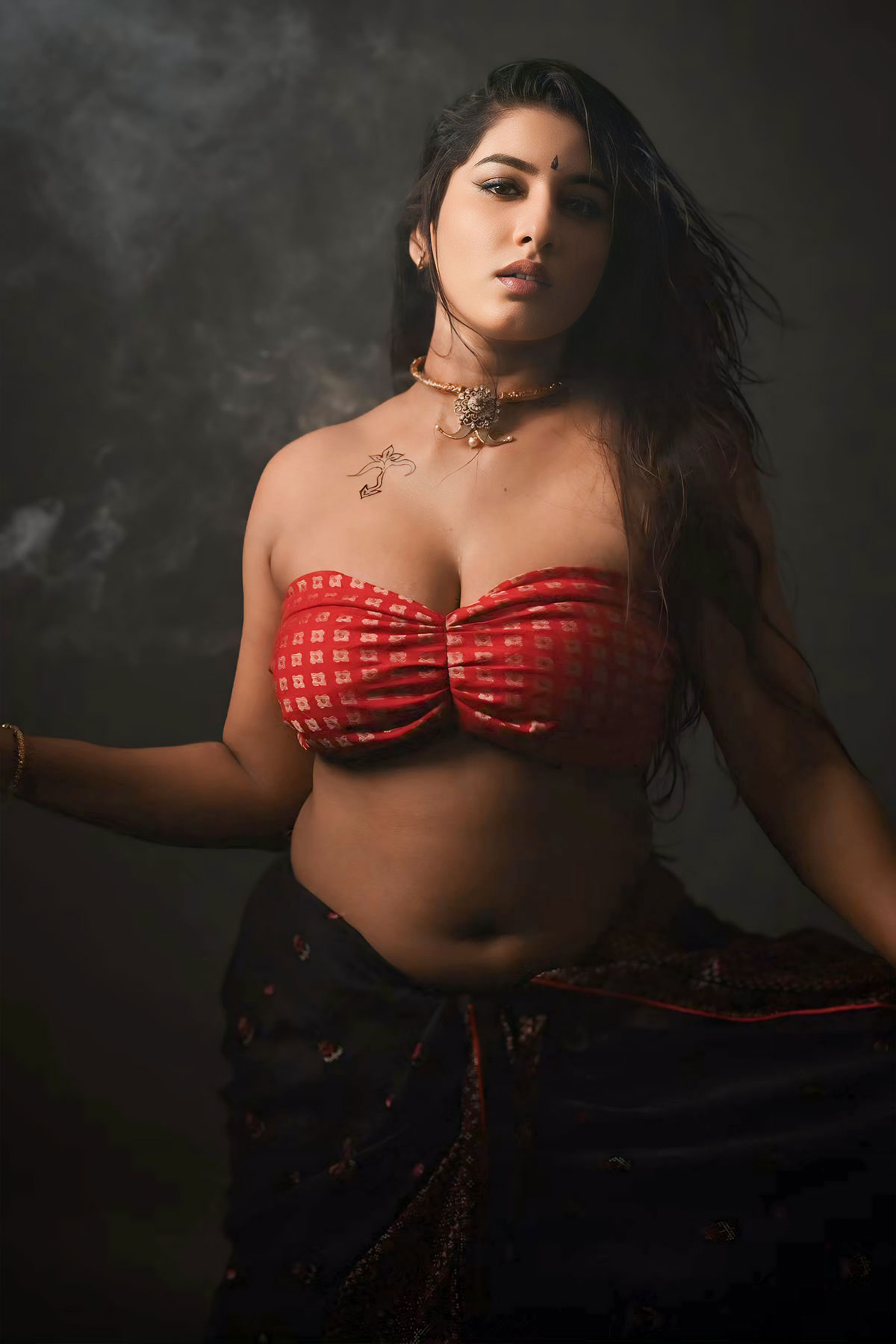 Vishnupriya, a curvy Indian woman in a red patterned bandeau tube top and black skirt with a chest tattoo.