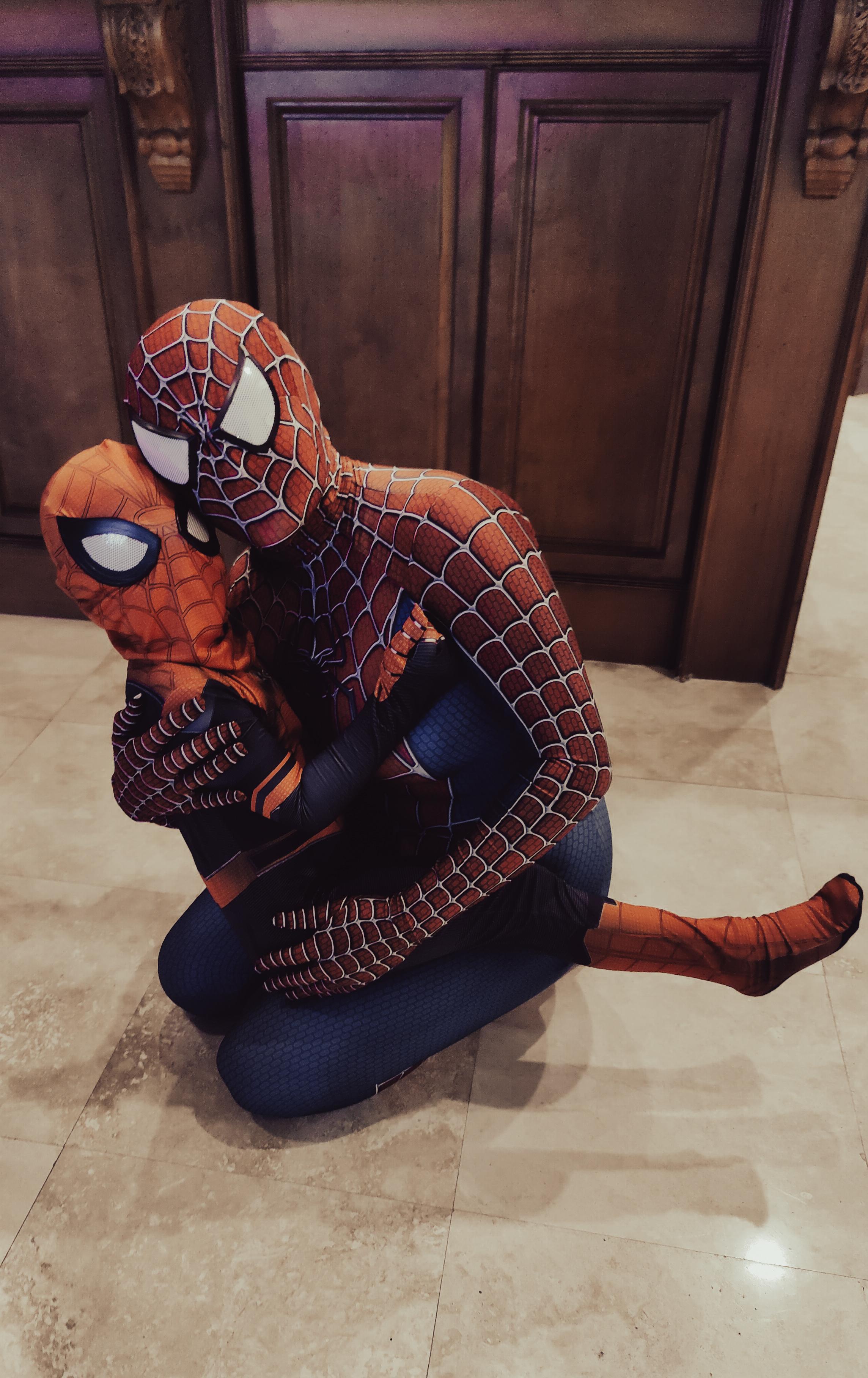 Two people in full-body red and blue Spider-Man costumes hugging on a tiled floor