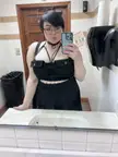 Curvy white goth girl with short black hair and glasses in a black strappy top and skirt taking a mirror selfie