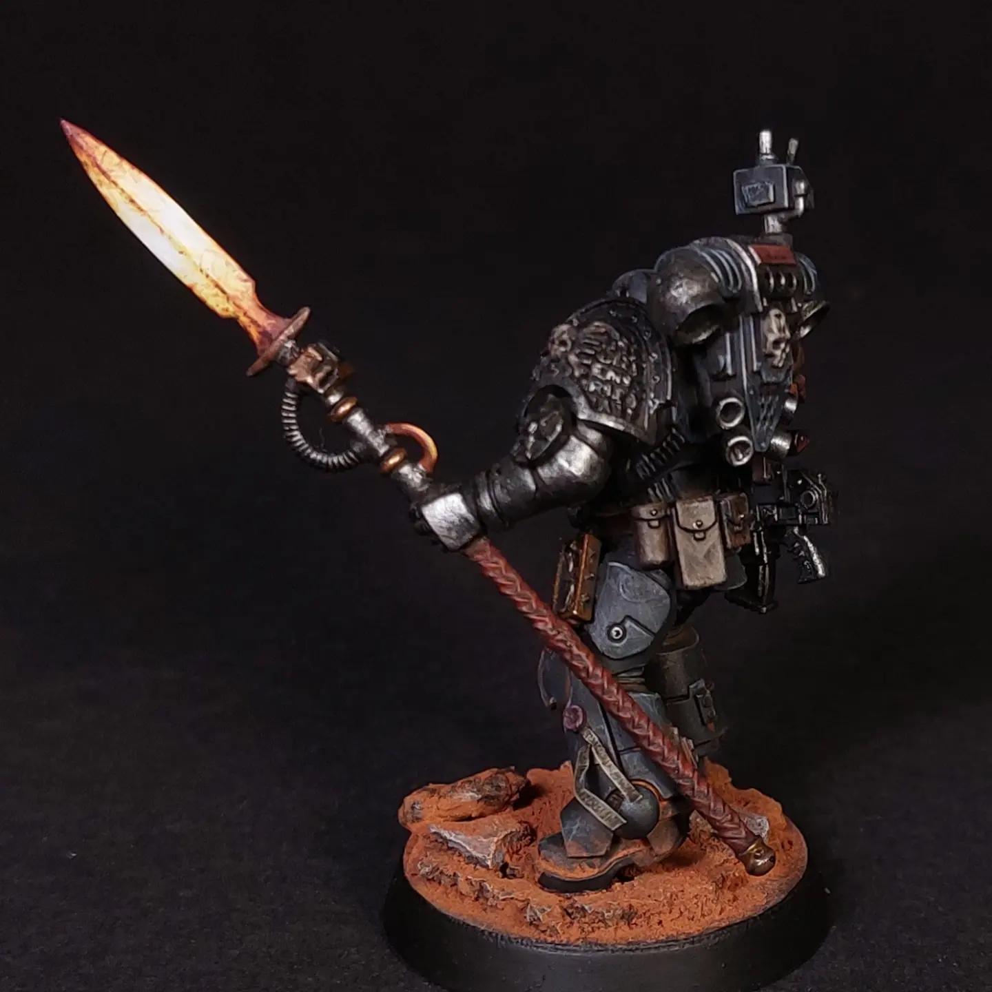 Kitbashed Deathwatch veteran miniature in dark grey armor with a glowing orange sword and gun on a rocky base