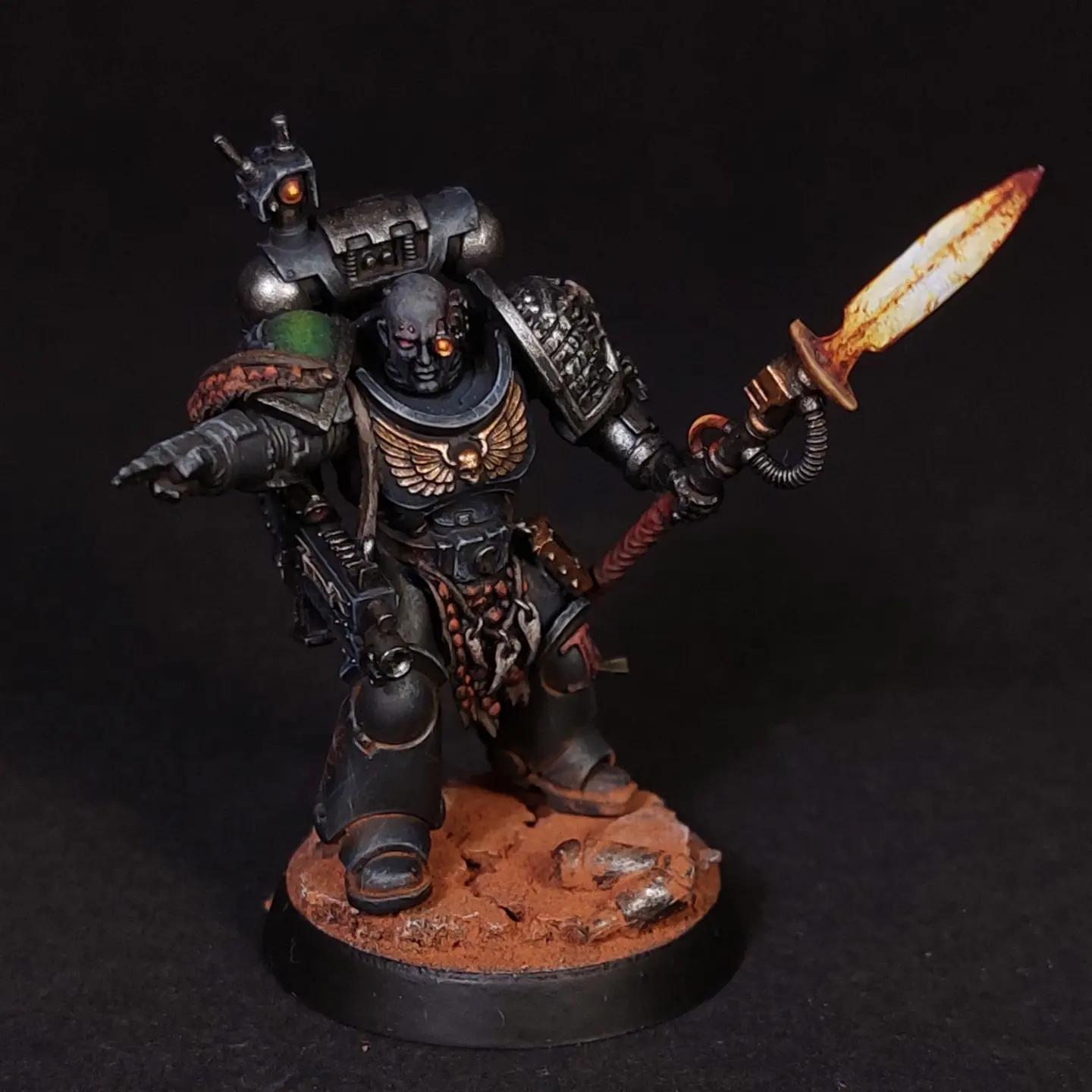 Kitbashed Deathwatch veteran miniature in dark grey armor with a glowing orange sword and gun on a rocky base