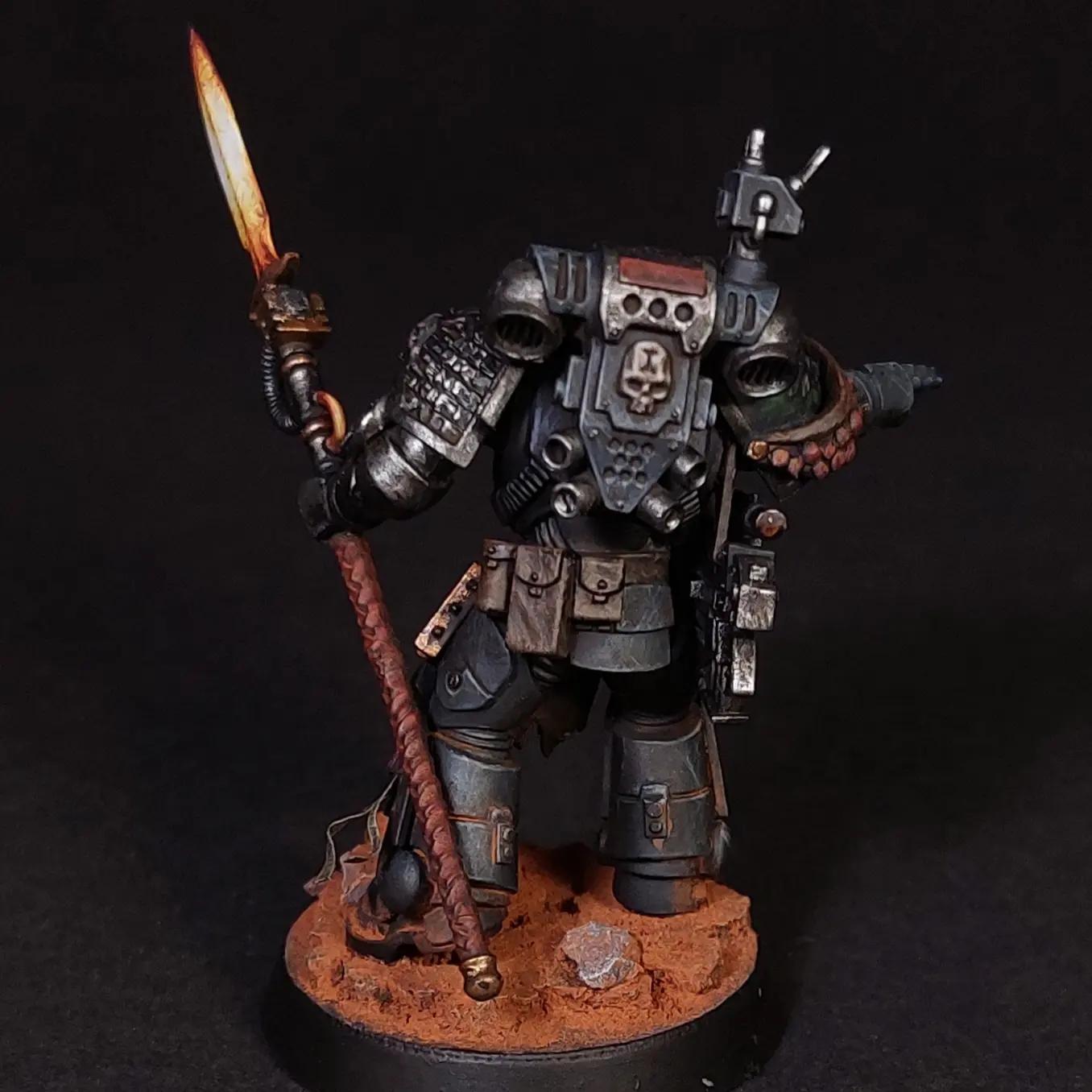 Kitbashed Deathwatch veteran miniature in dark grey armor with a glowing orange sword and gun on a rocky base