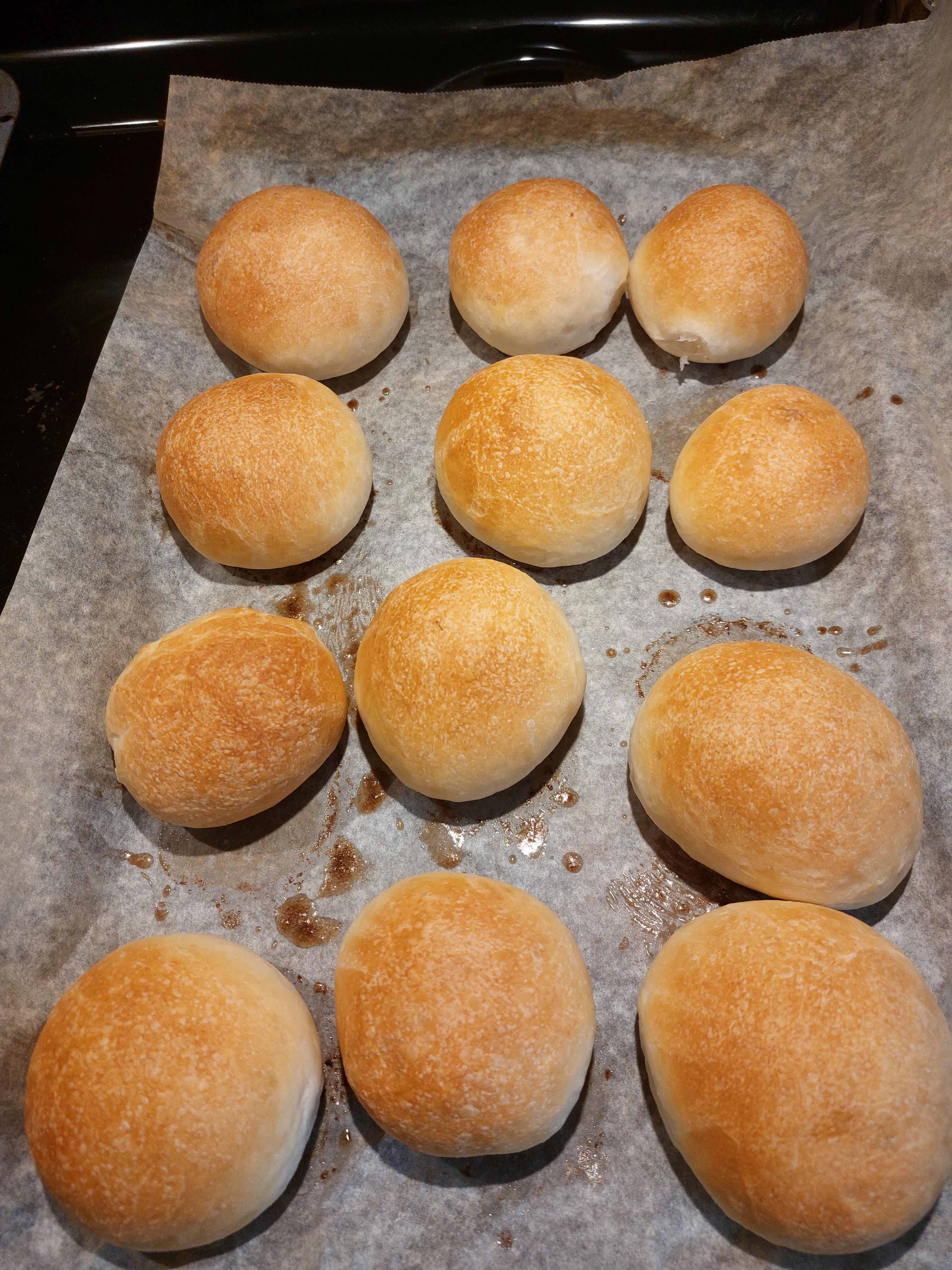 Homemade dinner rolls on a baking sheet and one served with a bowl of soup on a floral print surface.