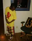 A Juggalo in a yellow t-shirt and colorful plaid shorts looking down in a living room.