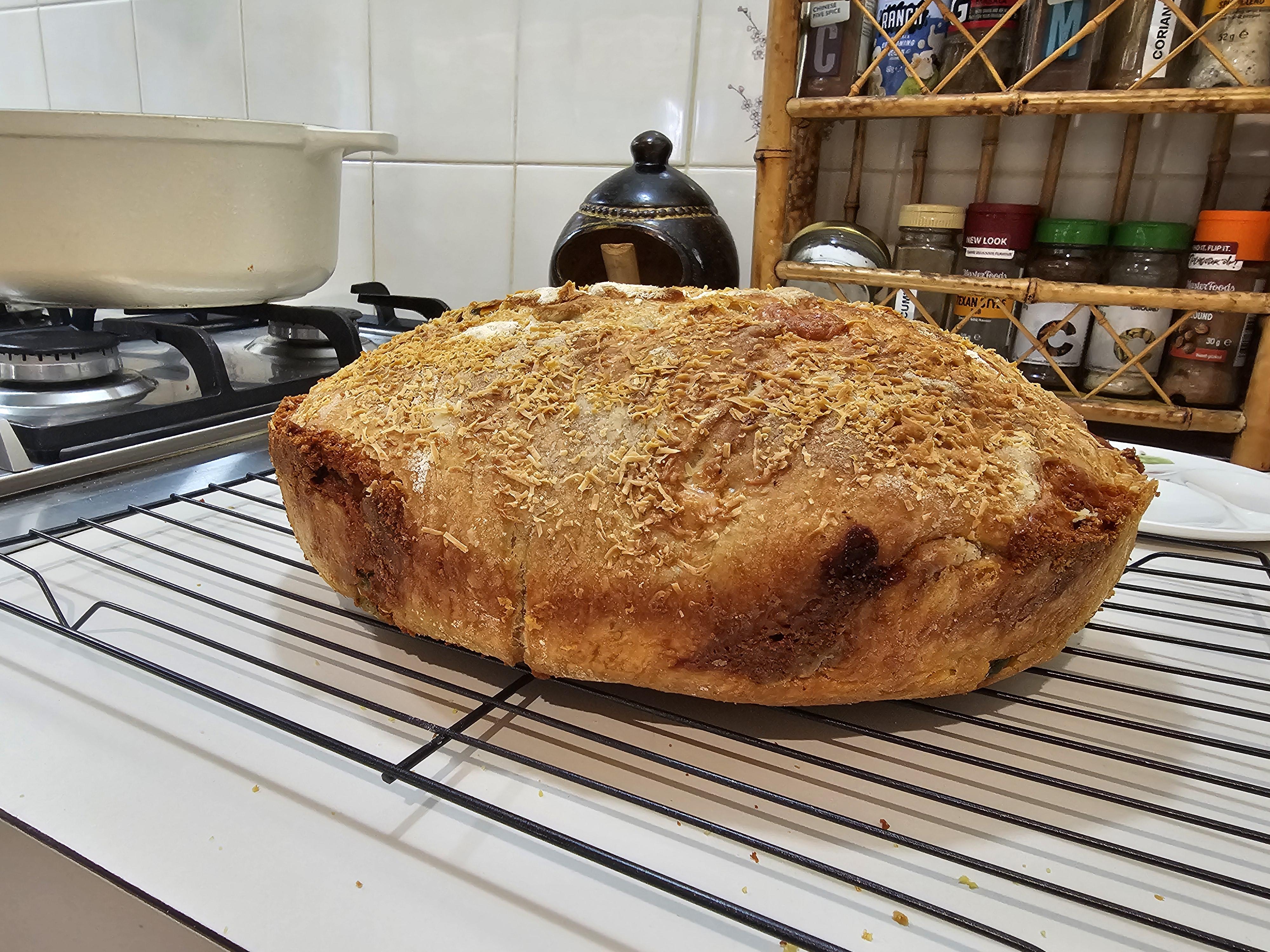 Jalapeno and cheese loaf of homemade bread being baked, cooled on a rack, and sliced by a hand with pale skin
