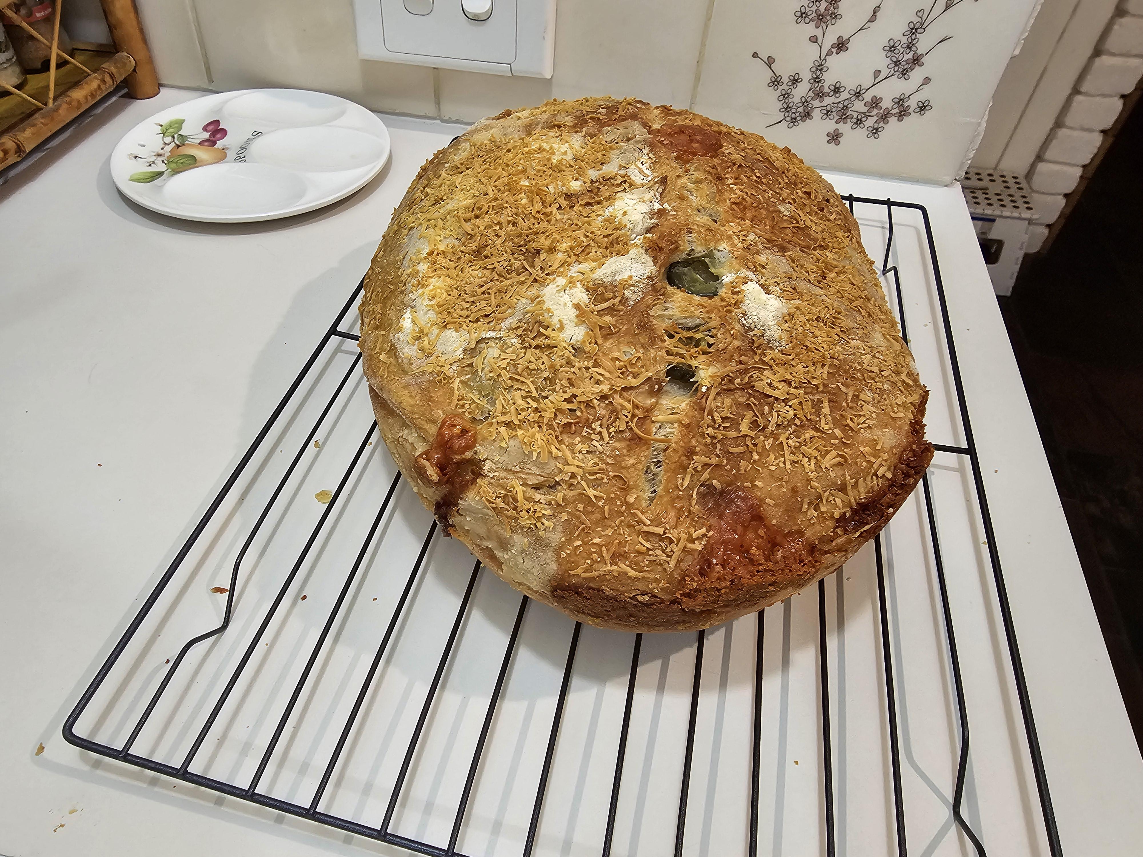 Jalapeno and cheese loaf of homemade bread being baked, cooled on a rack, and sliced by a hand with pale skin