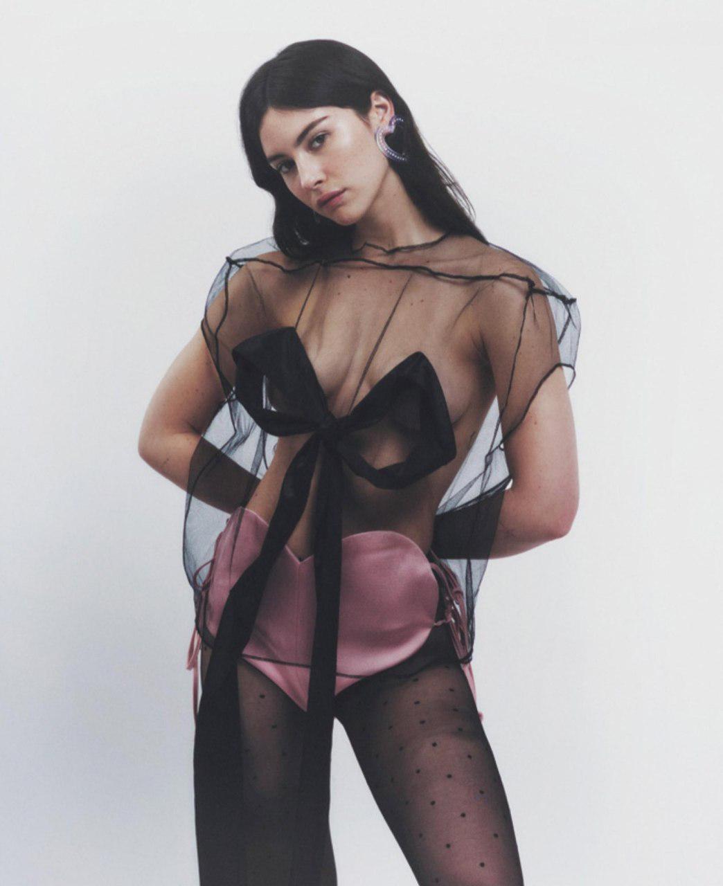 Gracie Abrams in a sheer black top with a bow, pink satin bottoms, and black polka dot tights