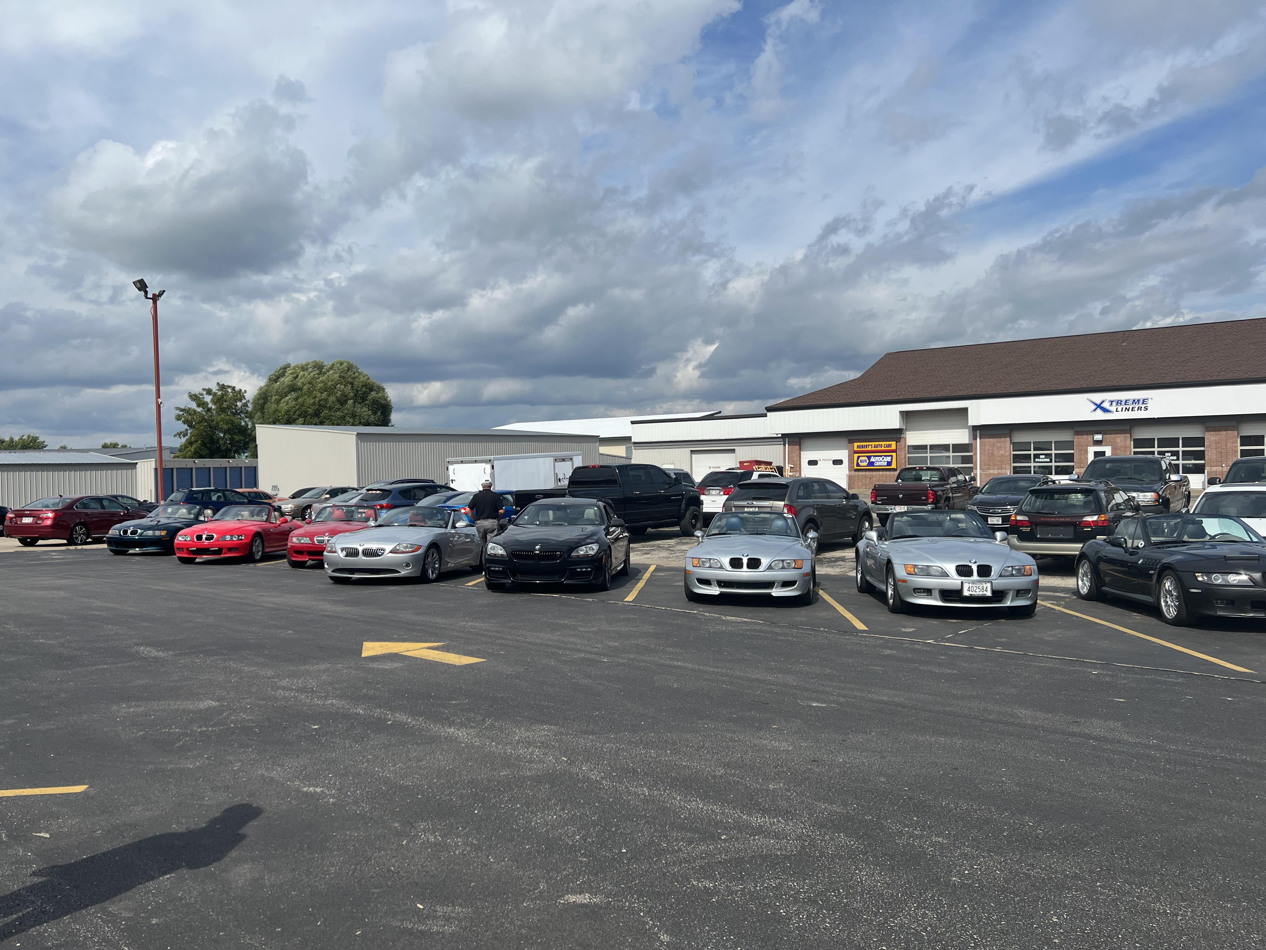 BMW Z series cars and a group of people in a gravel lot by a rocky cliff and forest