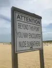 A wooden sign on the sandy shore of Gunnison Beach, New Jersey, warning of sunbathers ahead.