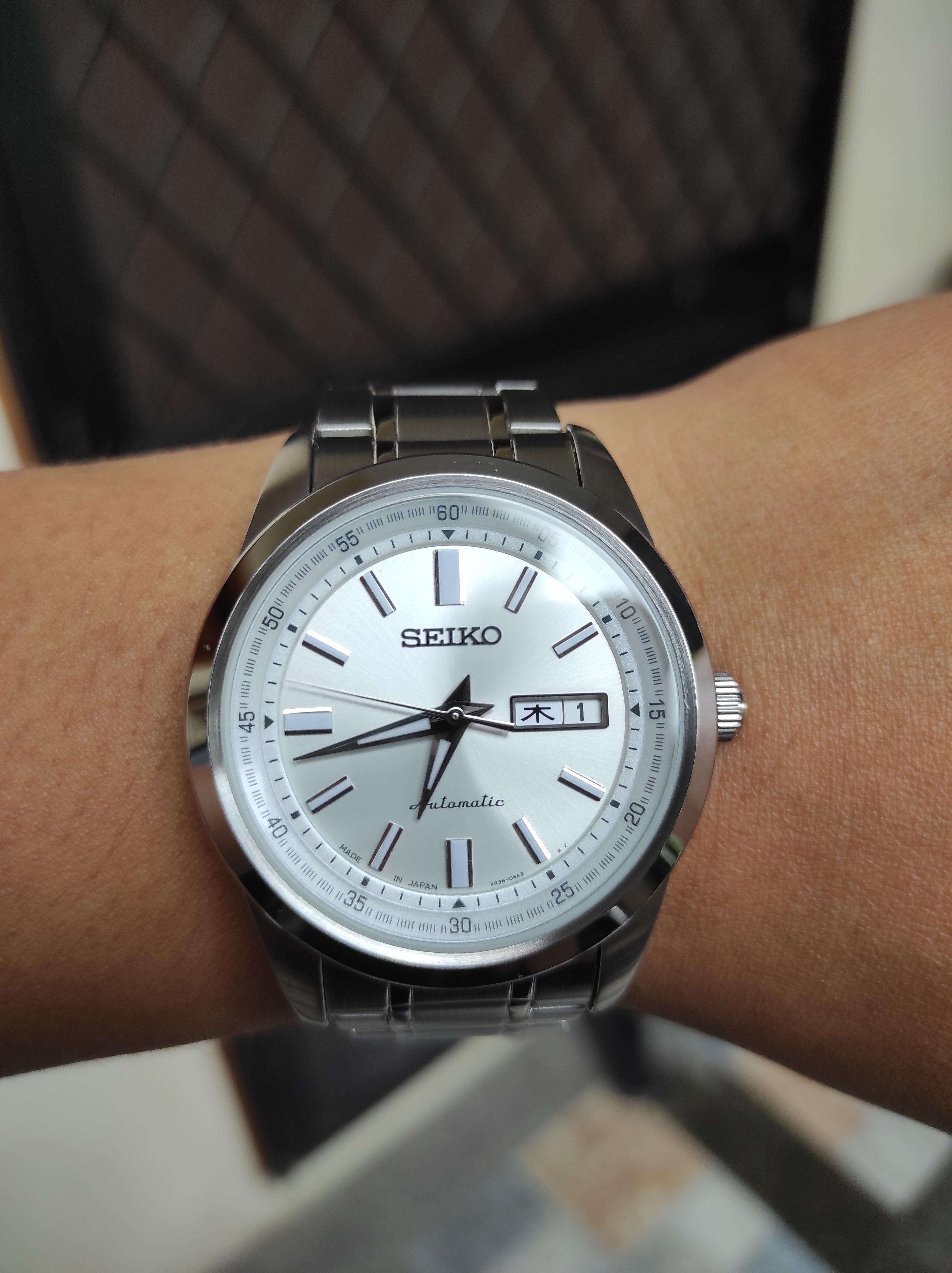 Silver Seiko automatic watch on a medium skin tone wrist, showing close-up details in daylight and dark settings.