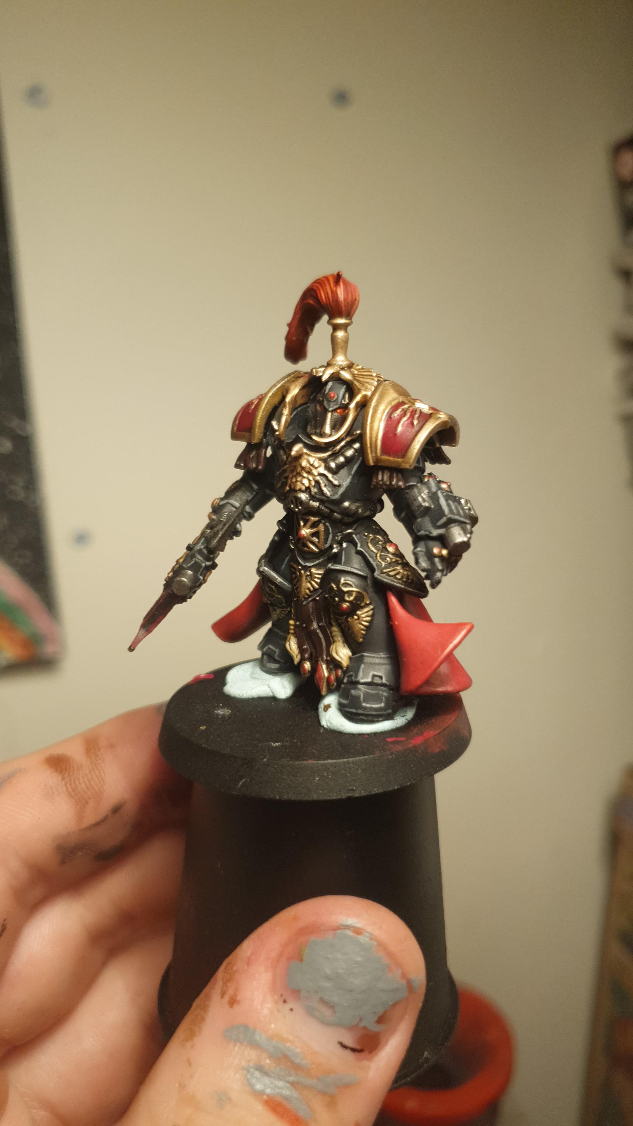 A hand holding a painted Warhammer miniature figure of a Shadowkeeper warrior with gold and red accents.