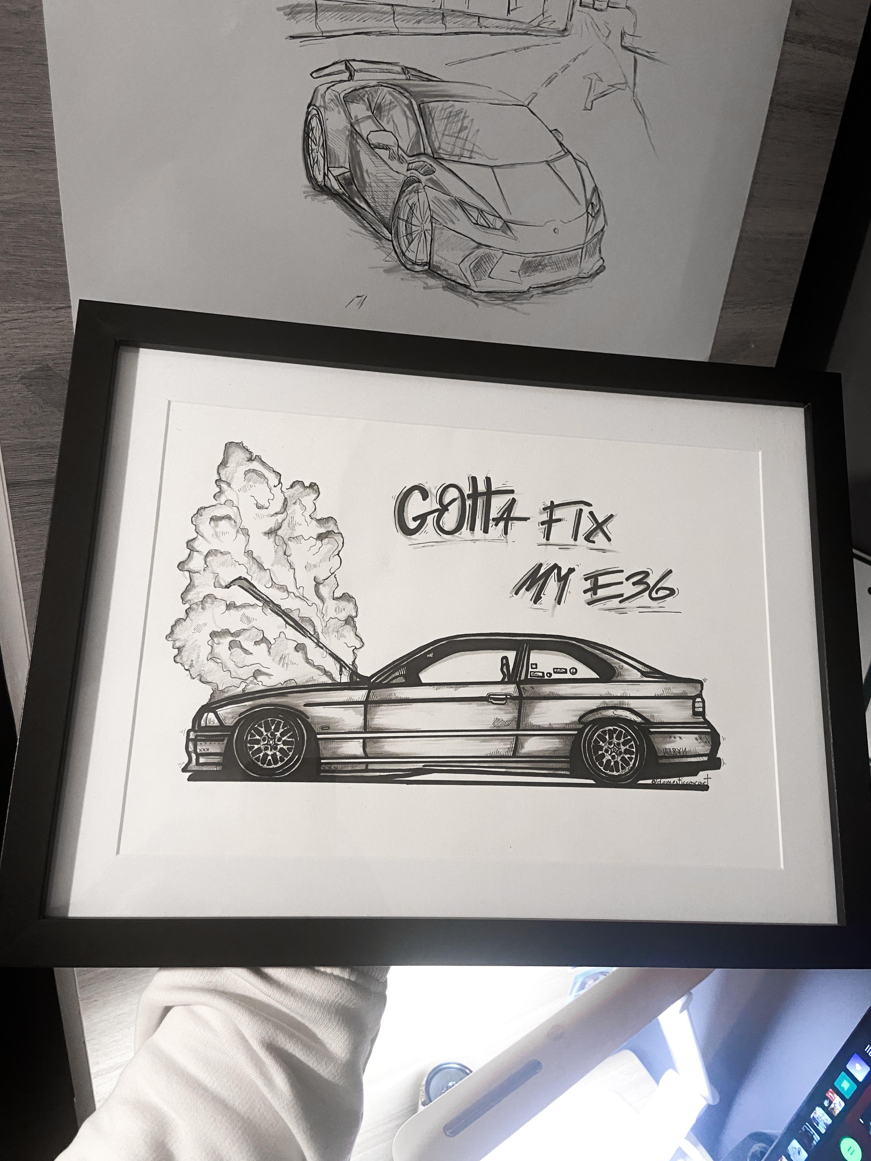 Person in a black glove holding a framed black and white BMW car concept art drawing in the snow