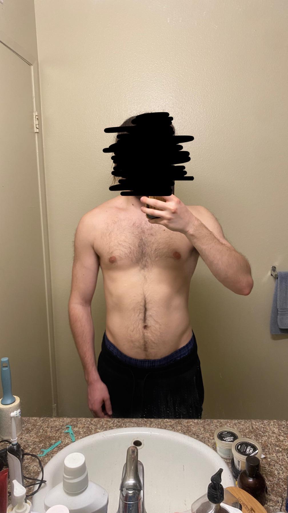 Shirtless white man in blue shorts posing for mirror selfies to show his bodybuilding physique in a bathroom