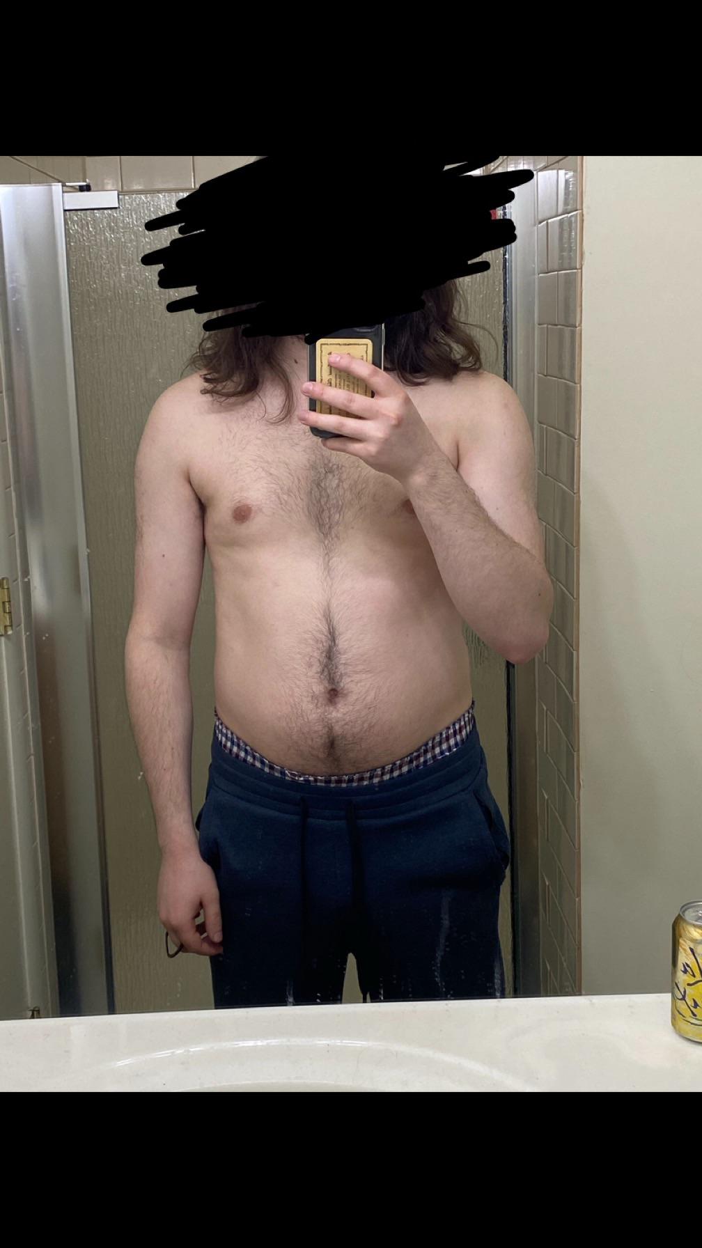 Shirtless white man in blue shorts posing for mirror selfies to show his bodybuilding physique in a bathroom