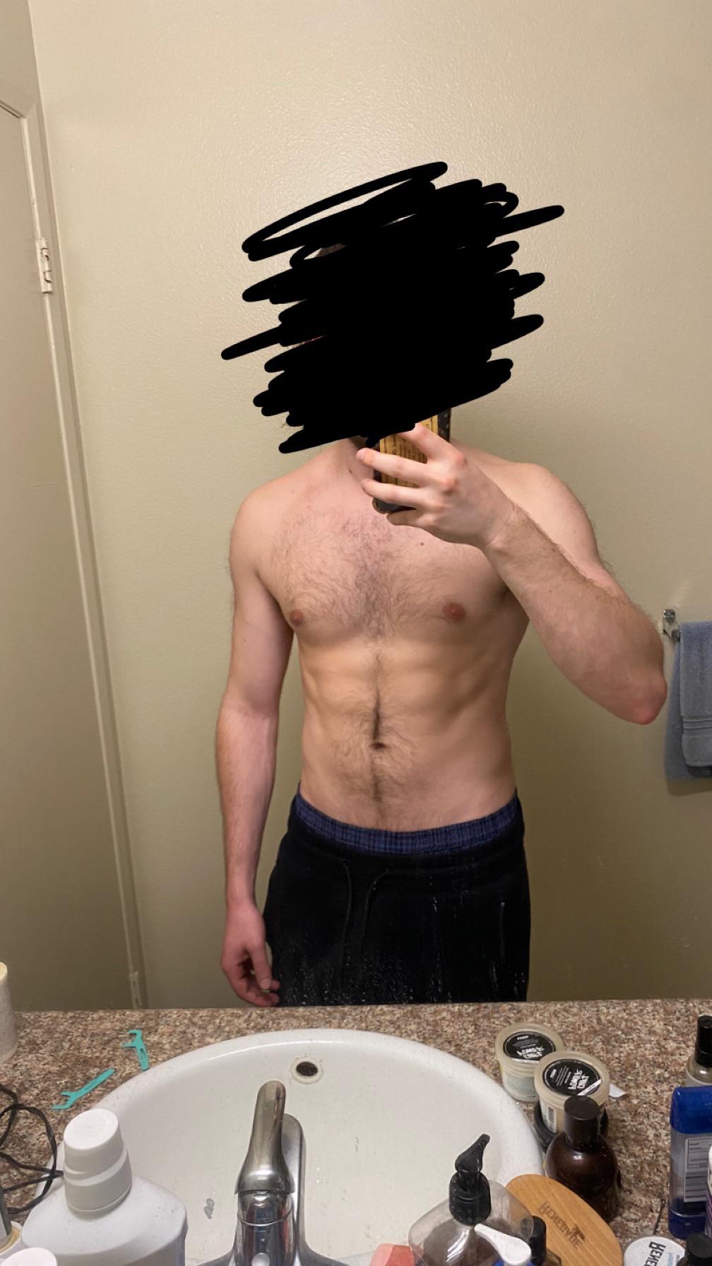 Shirtless white man in blue shorts posing for mirror selfies to show his bodybuilding physique in a bathroom