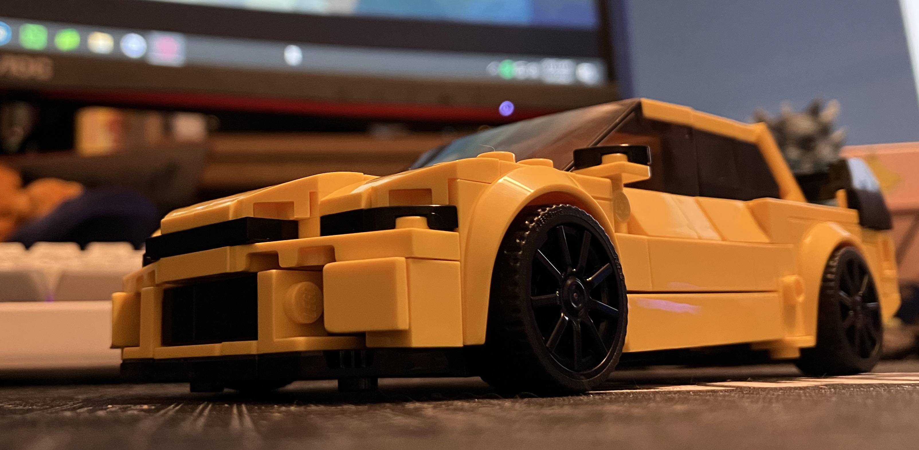 Yellow Lego Lancer sports car model on a gaming pc desk setup with a keyboard and desk mat