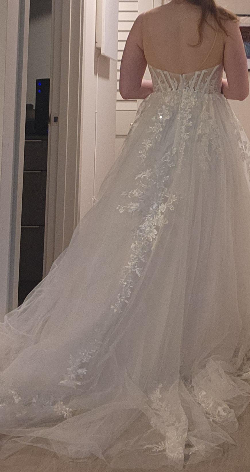 Woman with brown hair wearing a white lace wedding dress with a v-neck and sheer top