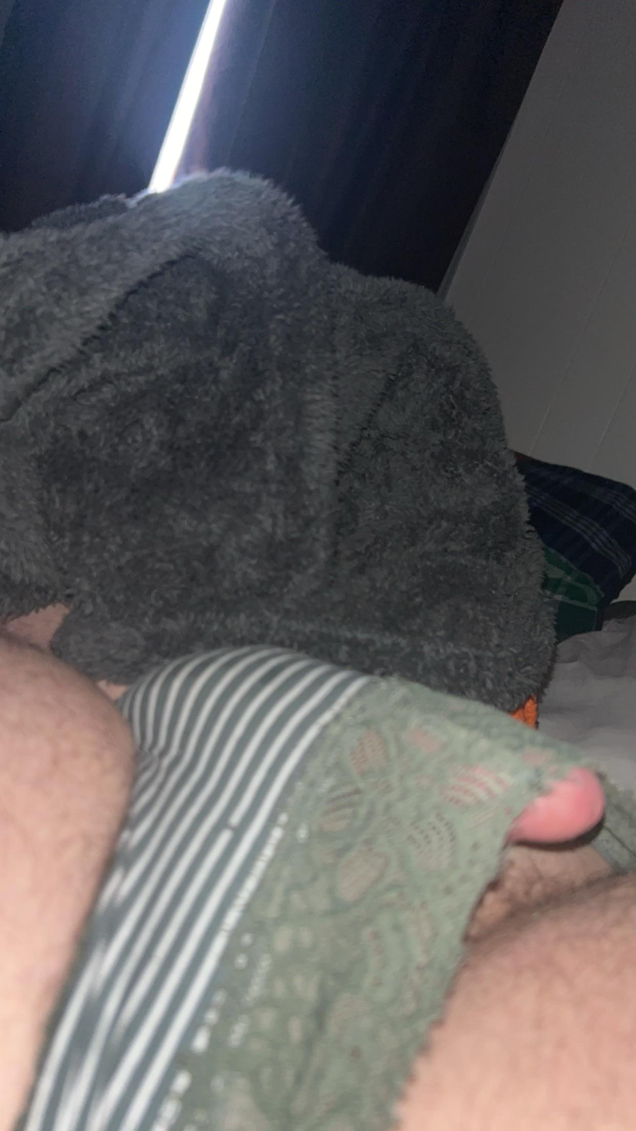 White man in striped underwear and green lace panties lying down in a bedroom, partially covered by a towel.