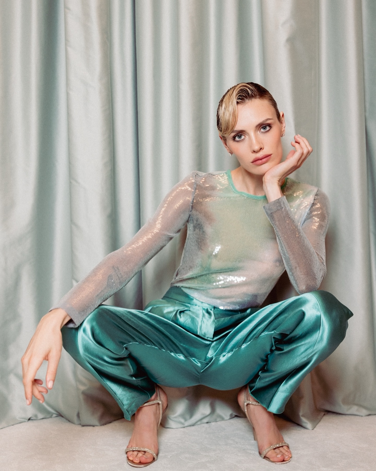 Wallis Day in a sheer silver sequined top and teal skirt standing with a man in a black suit