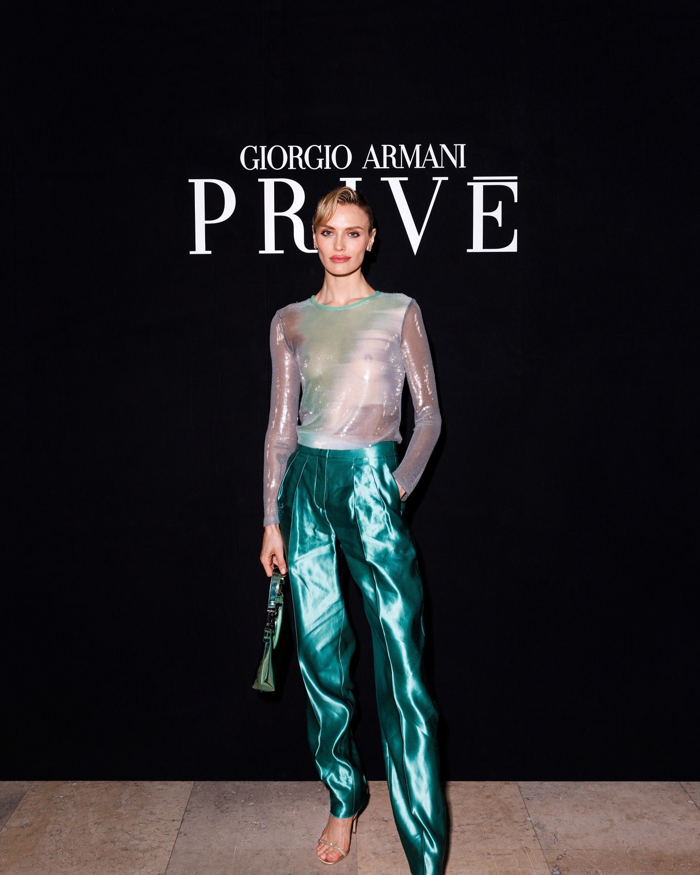 Wallis Day in a sheer silver sequined top and teal skirt standing with a man in a black suit