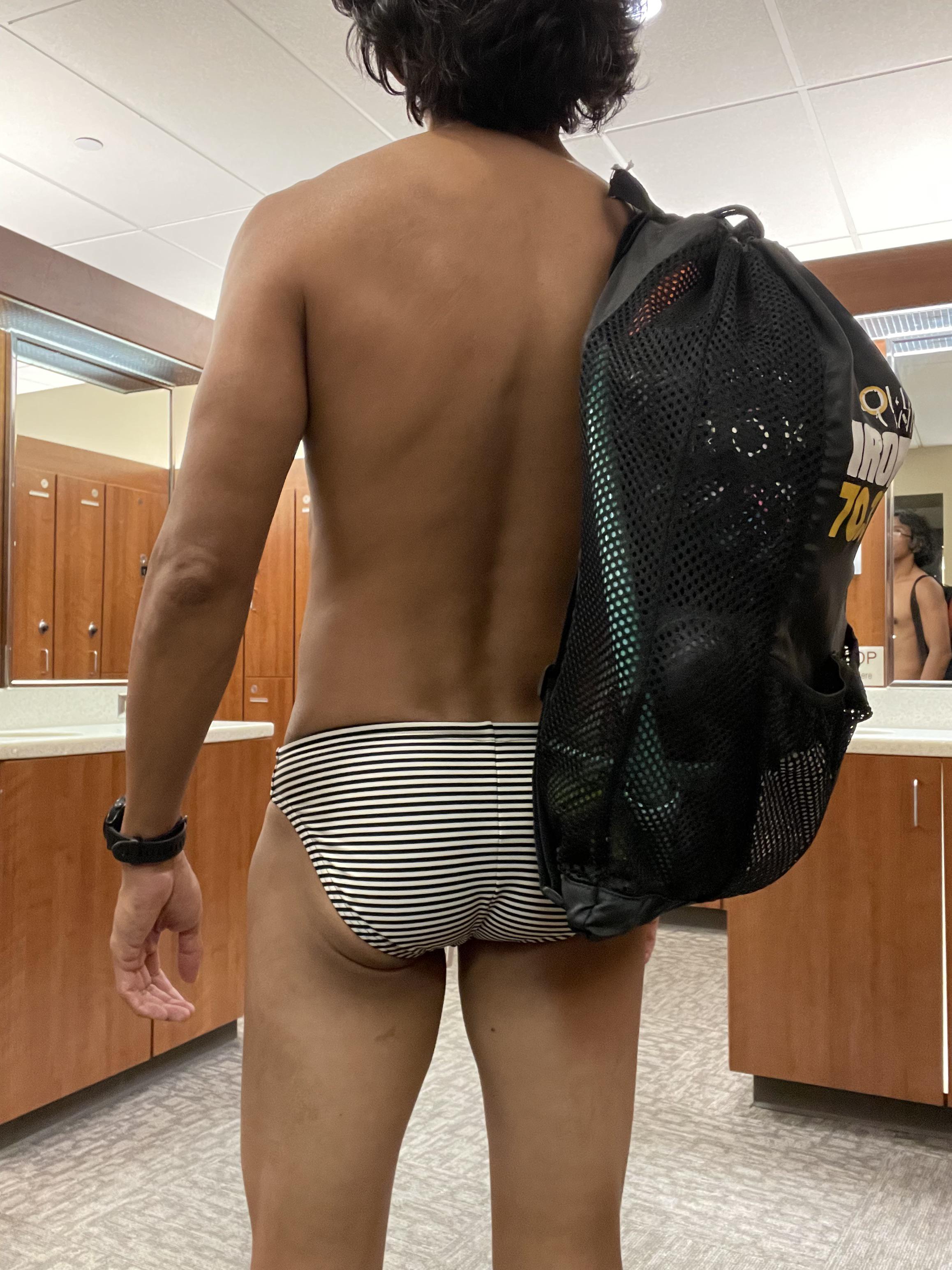 Athletic mixed man with curly hair posing in striped speedos in a locker room.