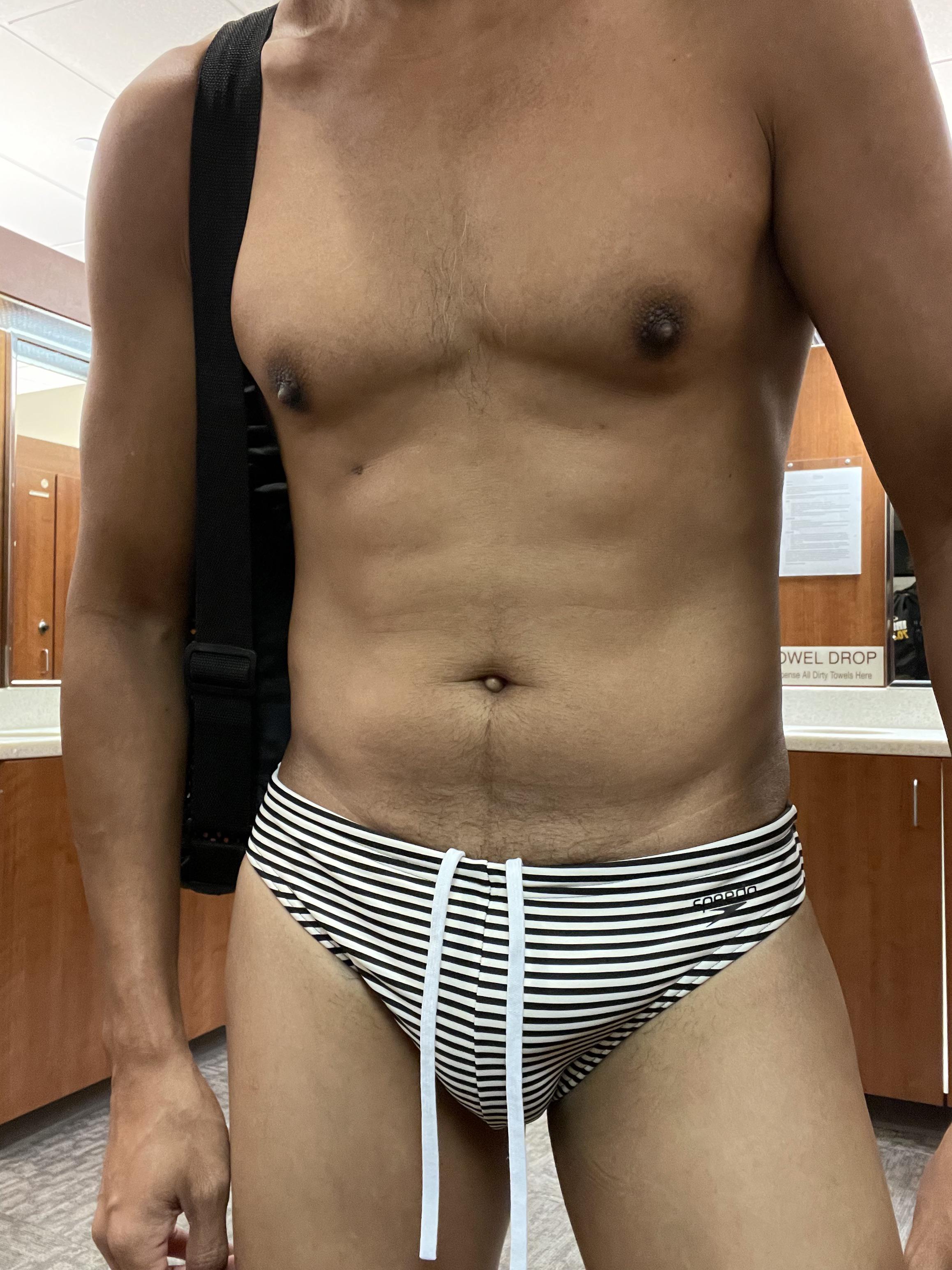 Athletic mixed man with curly hair posing in striped speedos in a locker room.