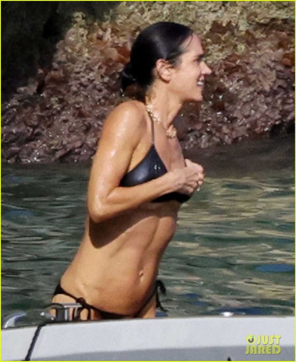 Muscled Jennifer Connelly in a black bikini swimming and climbing onto a boat in the ocean