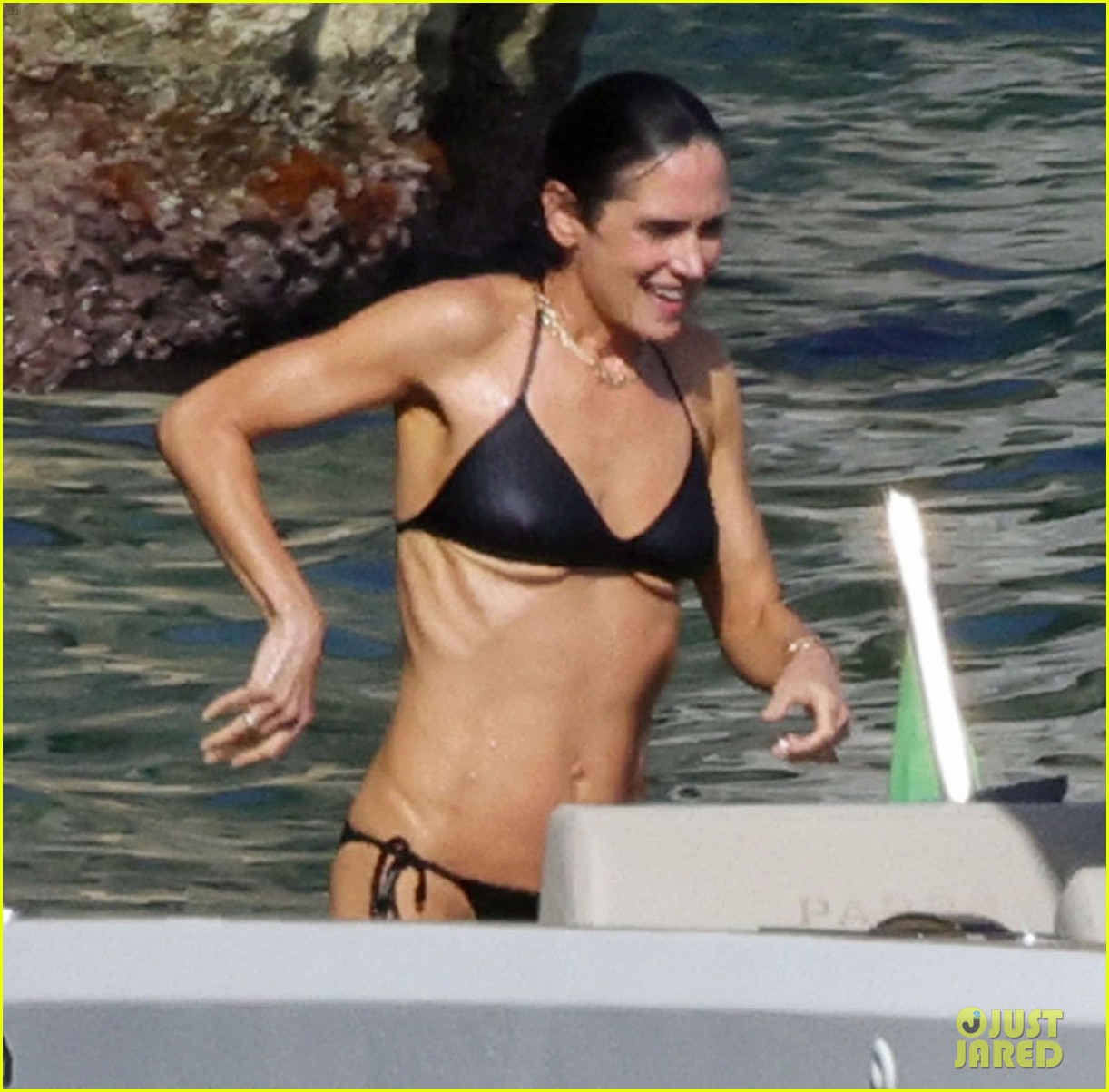 Muscled Jennifer Connelly in a black bikini swimming and climbing onto a boat in the ocean