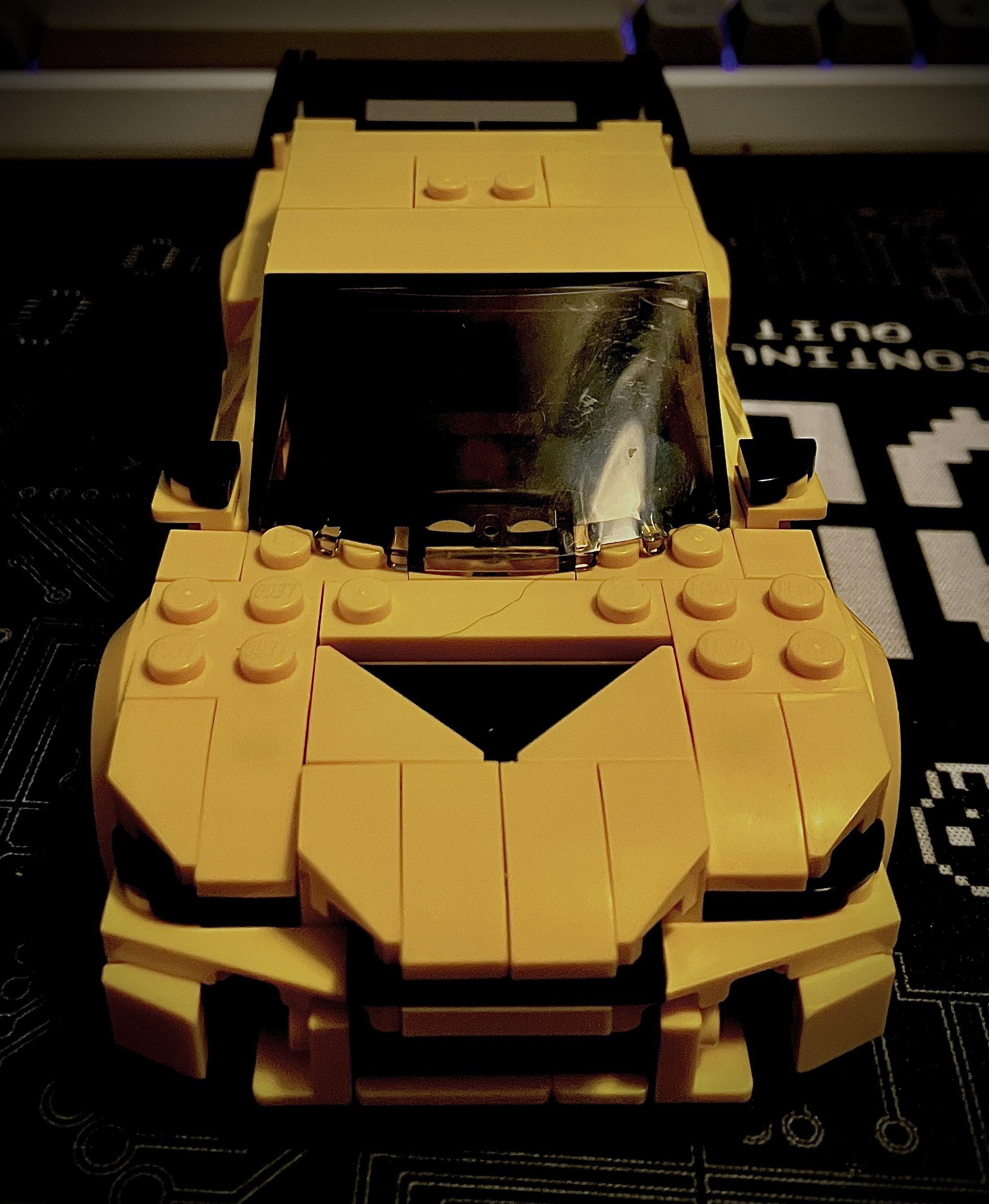 Yellow Lego Lancer sports car model on a gaming pc desk setup with a keyboard and desk mat