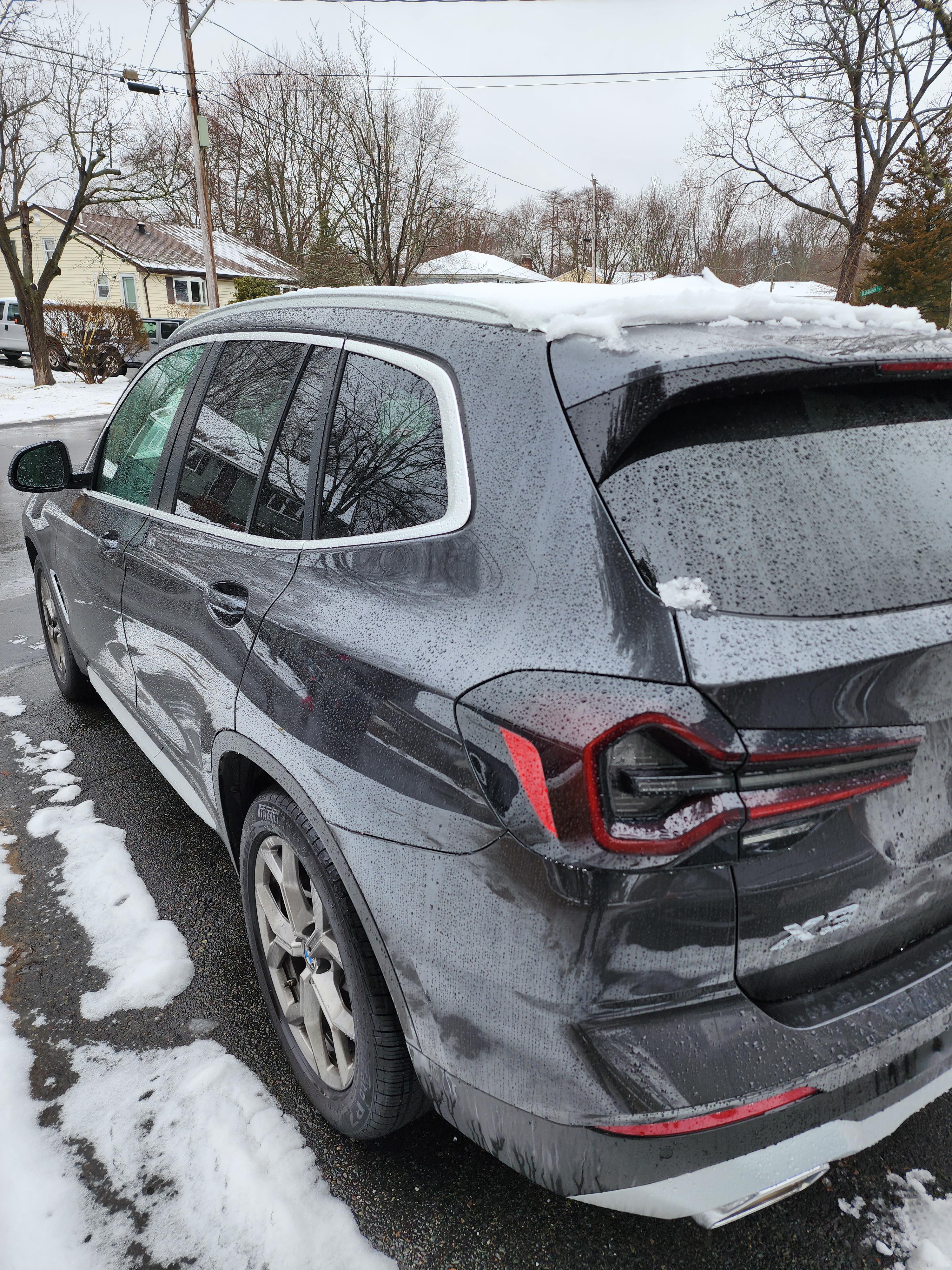 Grey BMW X3 SUV parked on a snowy residential street with snow on its roof