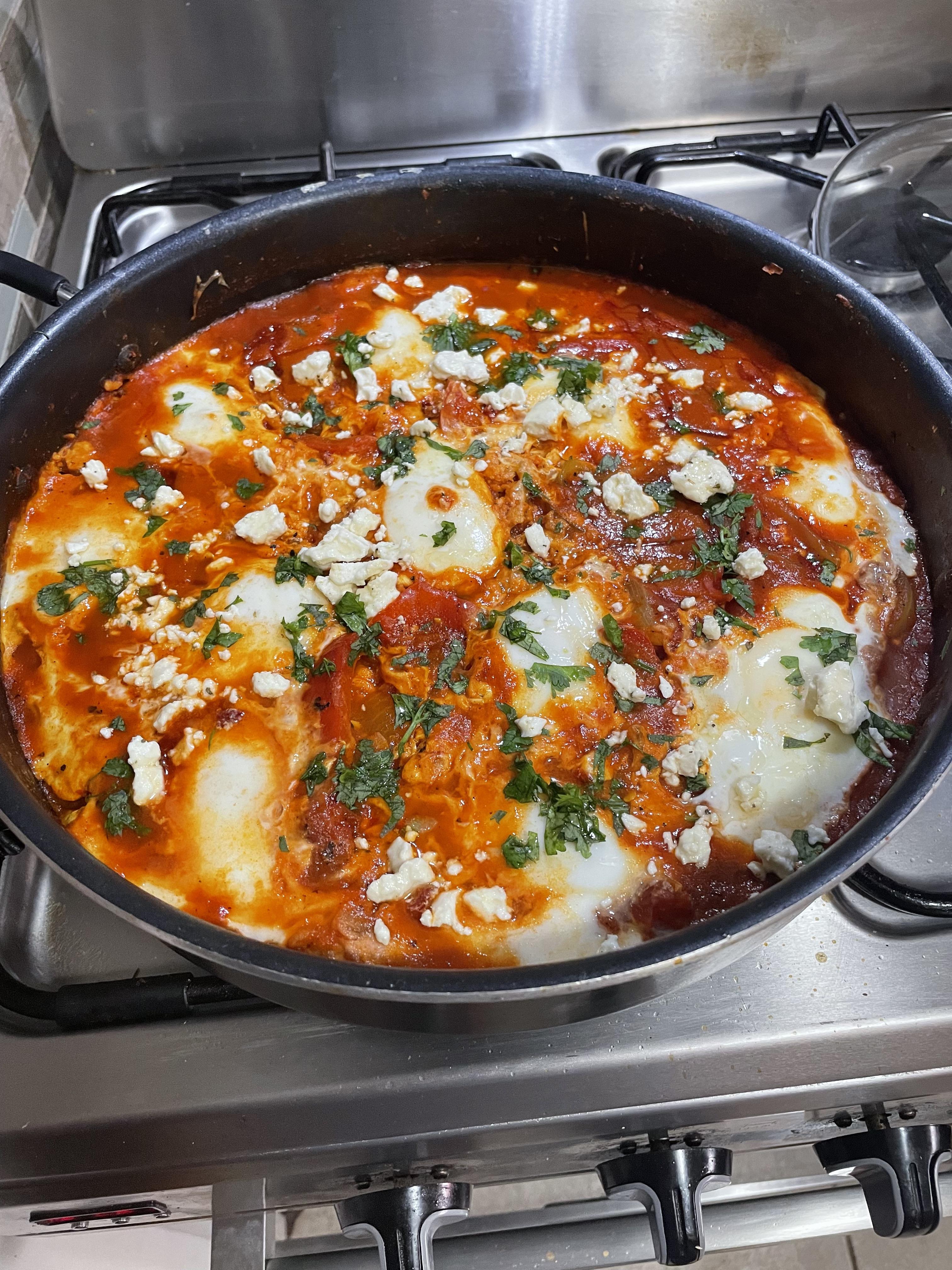 Homemade shakshuka with eggs on a white plate, served with pita bread and tzatziki on a wooden table.