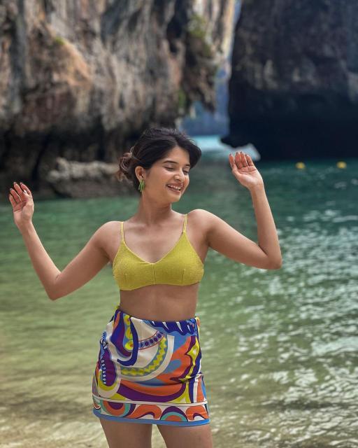 Bhavika Sharma in a red strapless satin dress, white bikini, and colorful tropical print swimwear at the beach.