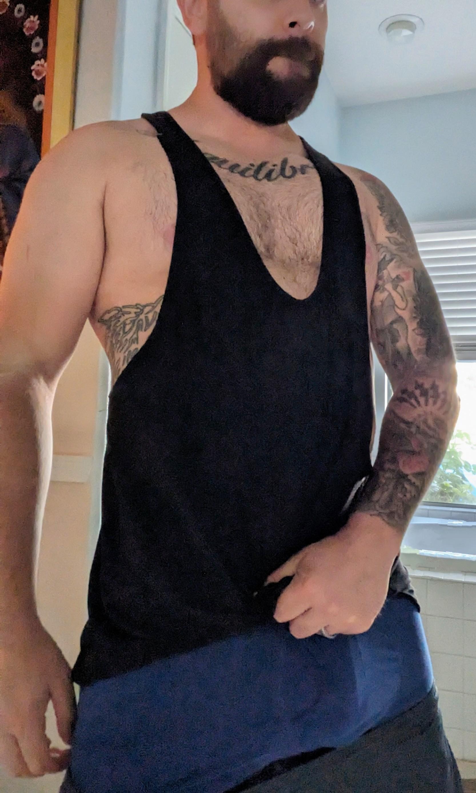 Muscular white man with tattoos in a black tank top and blue underwear performing a handjob