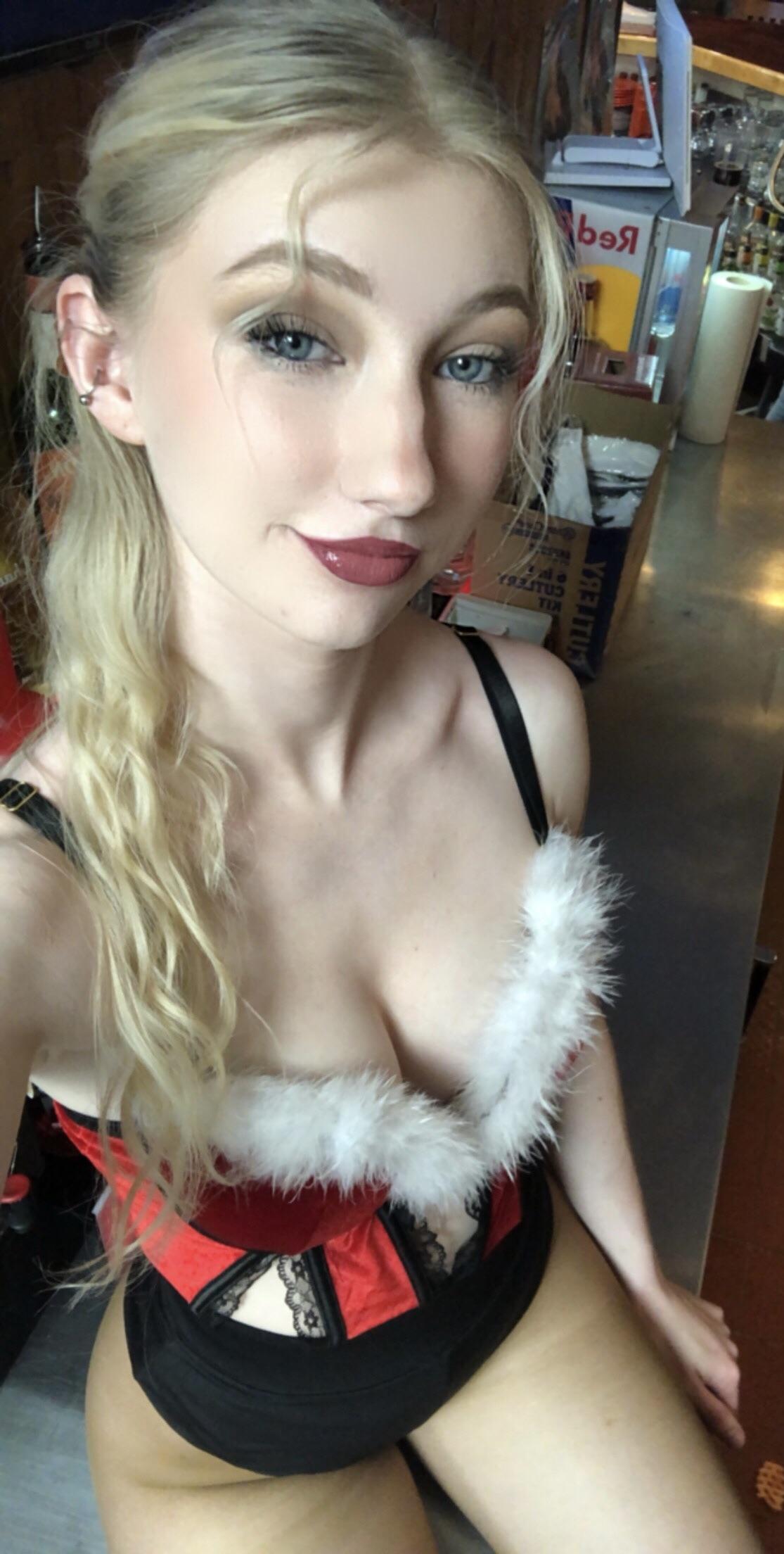 A slender woman with long blonde hair wearing a sexy Mrs. Claus red and black corset outfit with white faux fur trim.