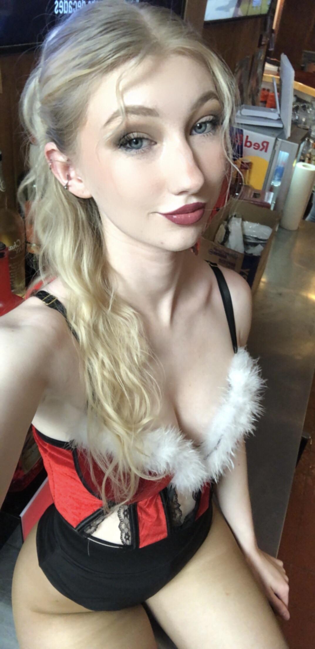 A slender woman with long blonde hair wearing a sexy Mrs. Claus red and black corset outfit with white faux fur trim.