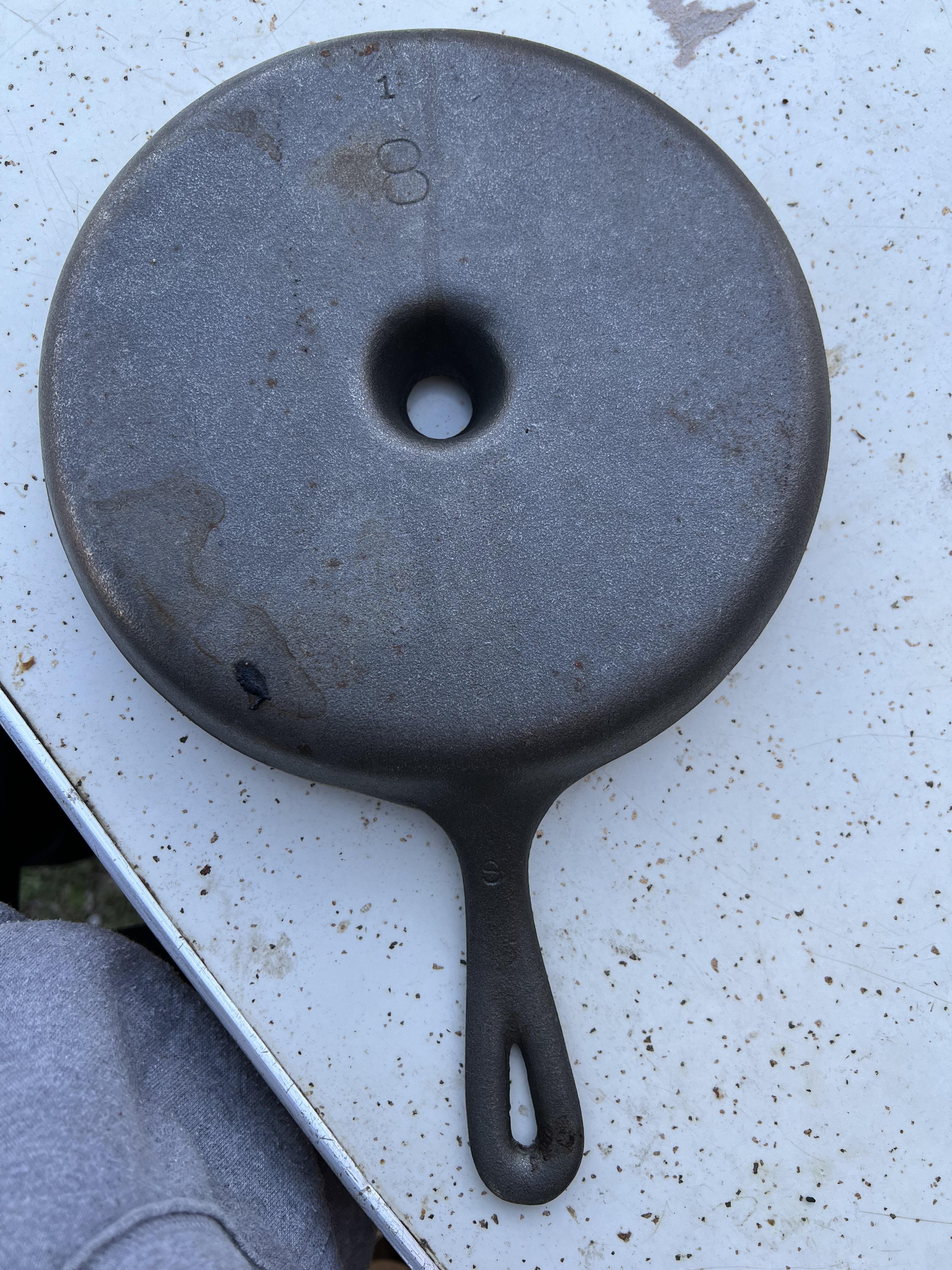 A white man in a grey sweatshirt holding a cast iron skillet with radial ribs and a central hole.