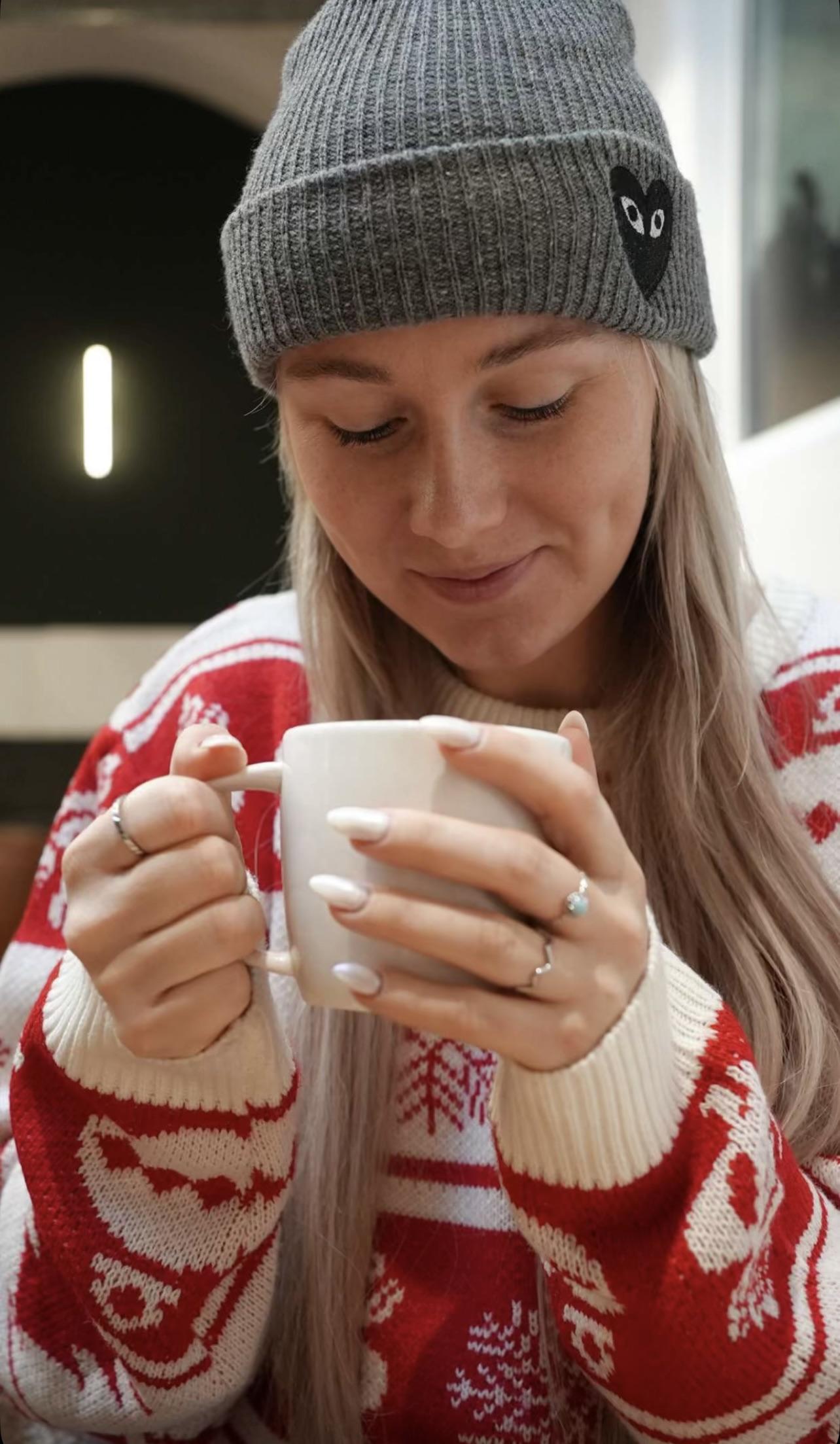Myron smiling in a red and white Christmas sweater and grey beanie, holding a white mug