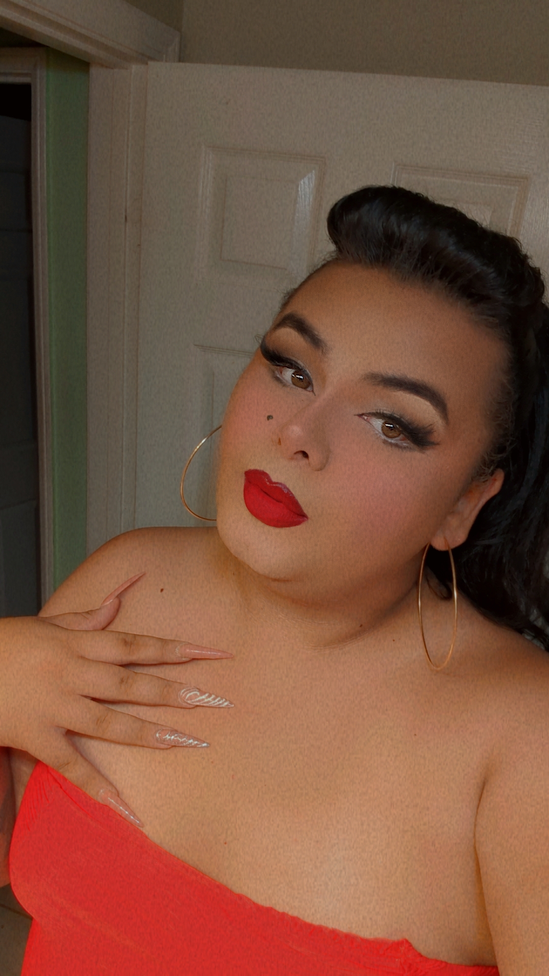 A plus-size trans person with light skin in a red top, brown halter top, and black clothing.