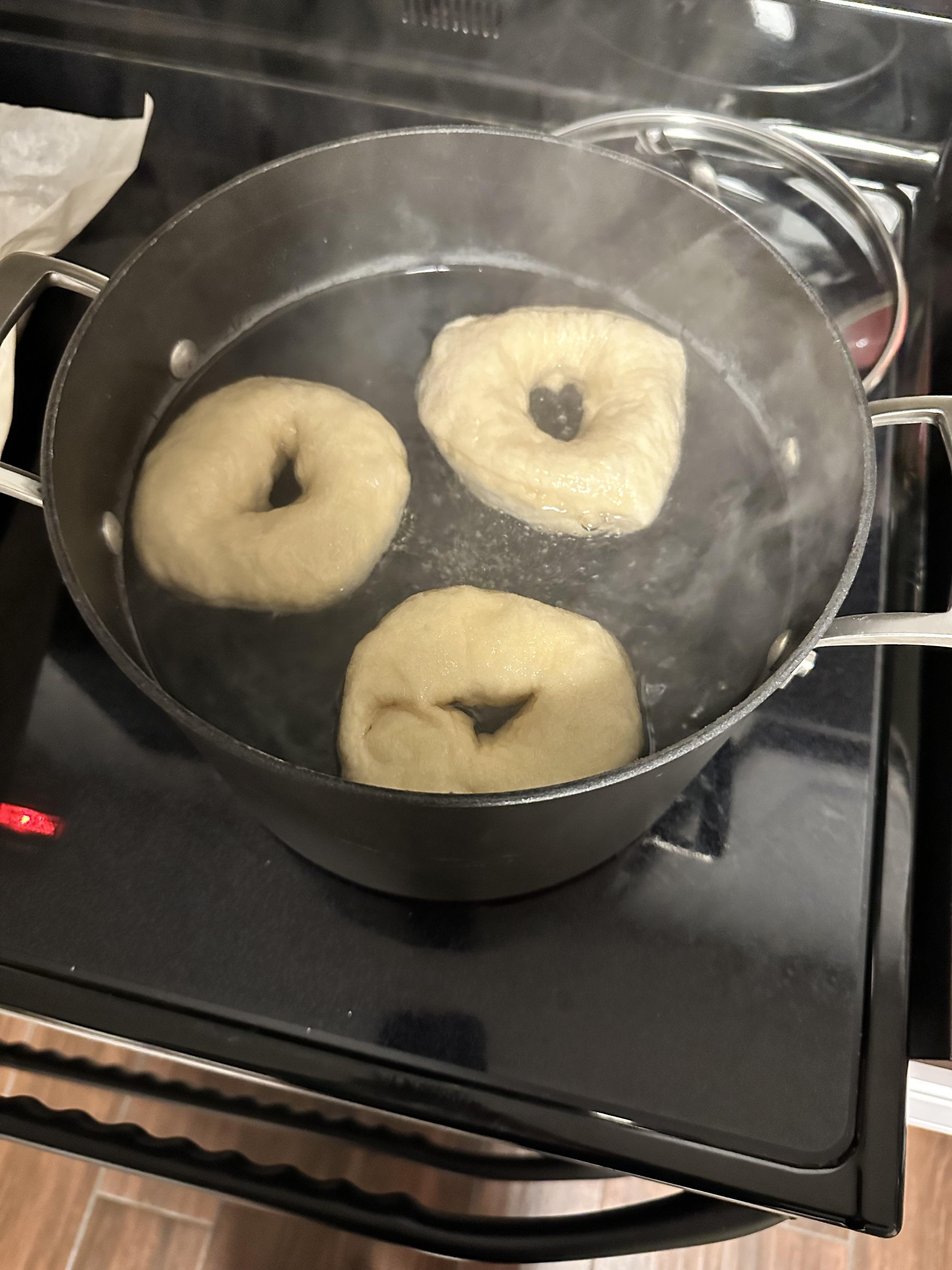 Homemade bagels on a cutting board in a kitchen, including a Cuisinart pot and a bagel sandwich.