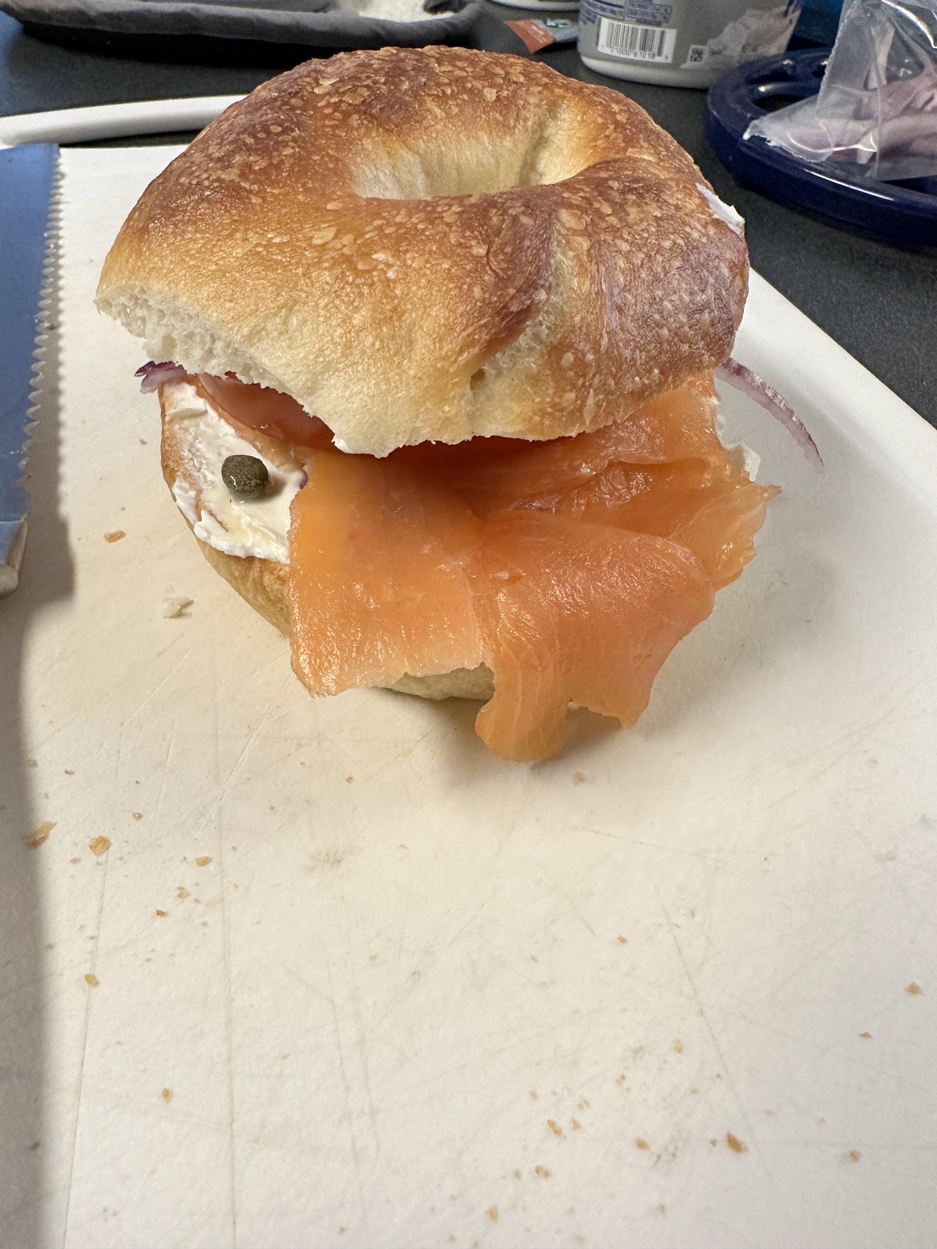 Homemade bagels on a cutting board in a kitchen, including a Cuisinart pot and a bagel sandwich.
