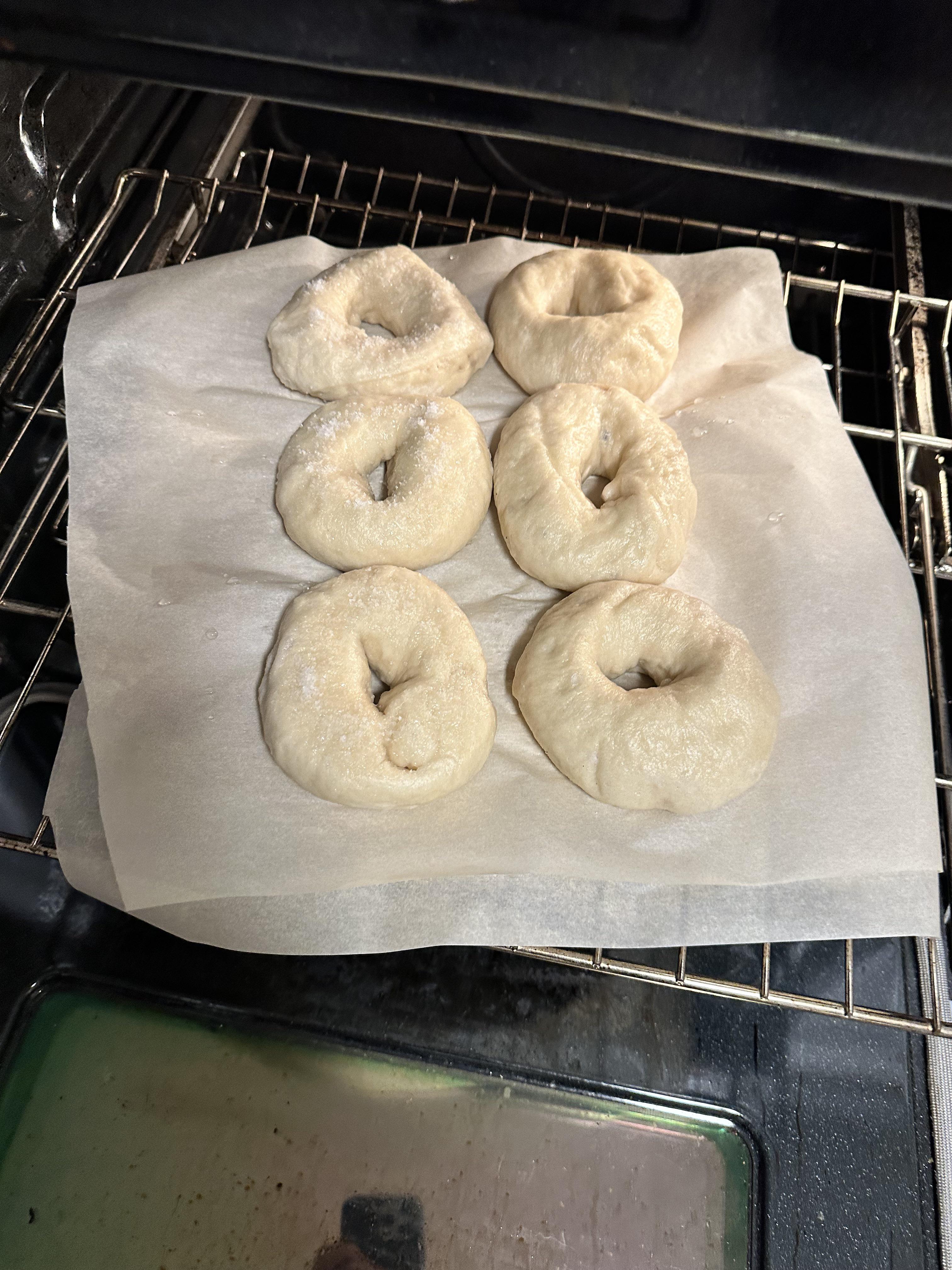 Homemade bagels on a cutting board in a kitchen, including a Cuisinart pot and a bagel sandwich.