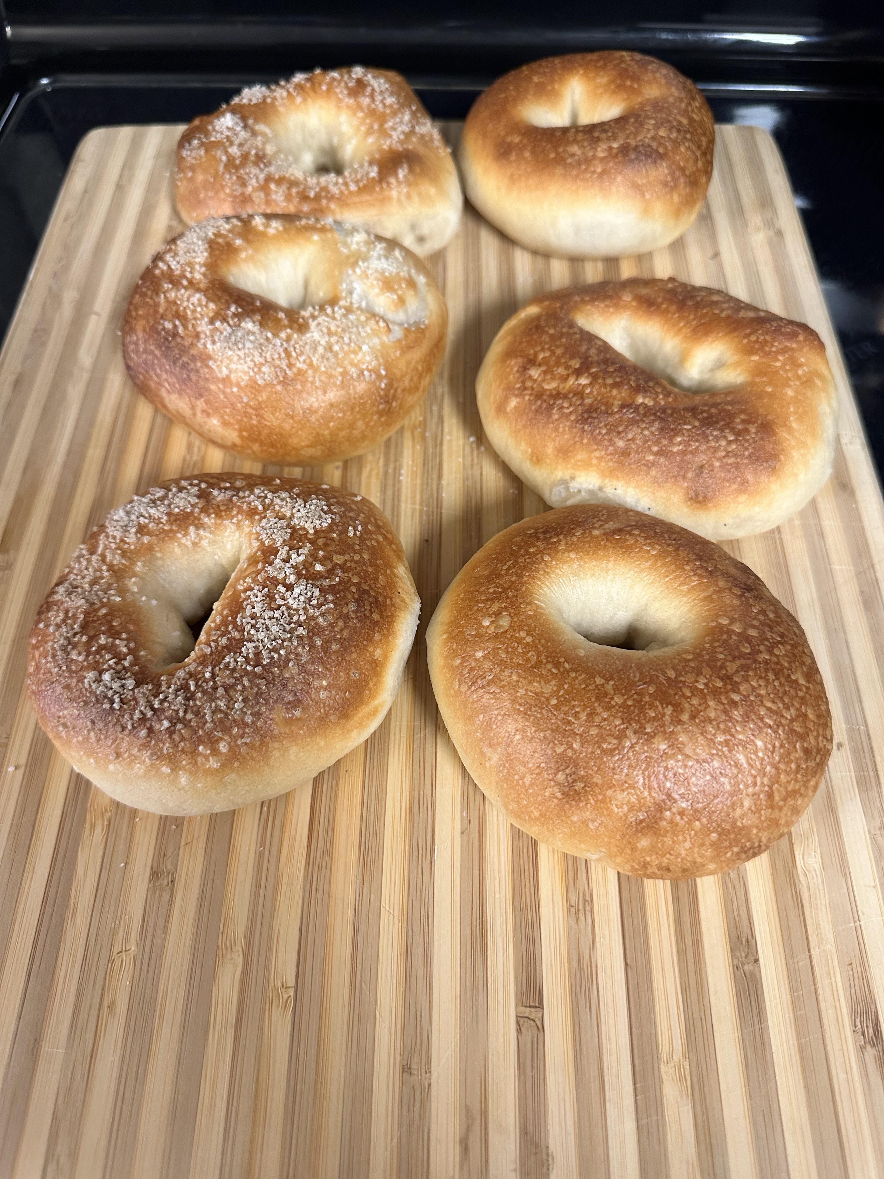 Homemade bagels on a cutting board in a kitchen, including a Cuisinart pot and a bagel sandwich.