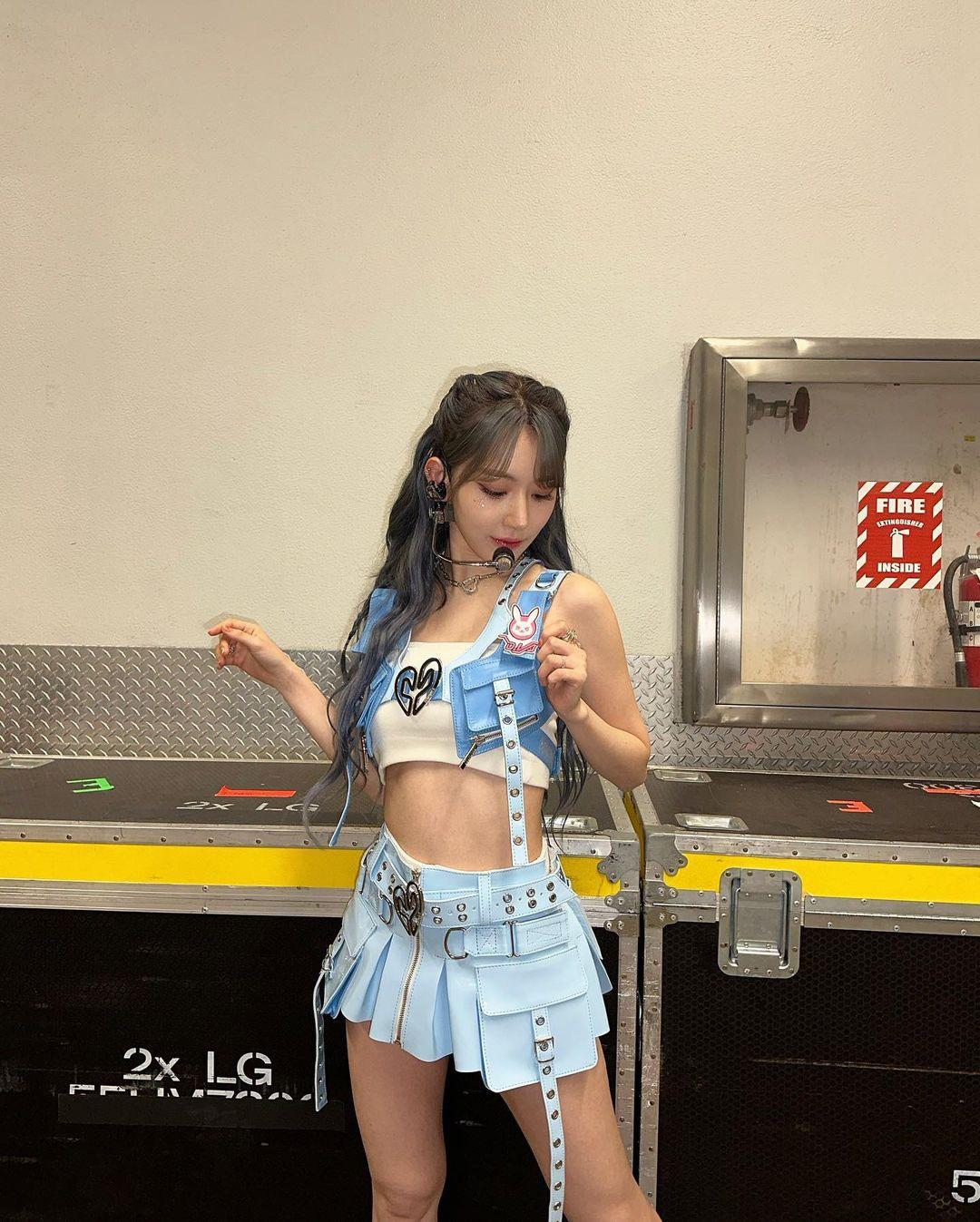 Sakura in a blue denim vest, white crop top, and short skirt with greyish-blue hair