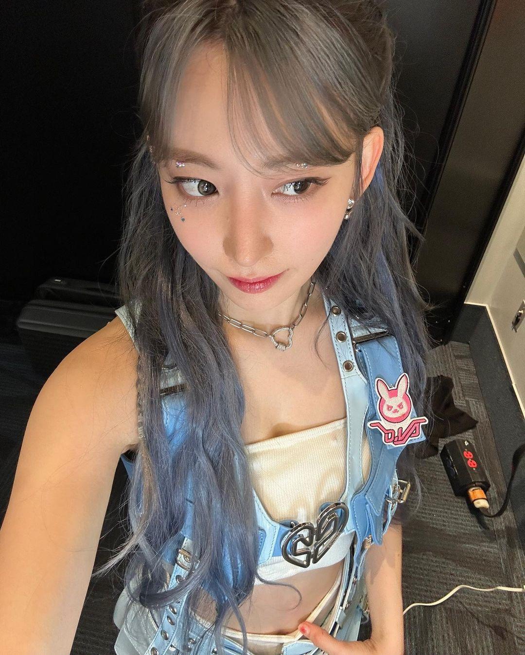 Sakura in a blue denim vest, white crop top, and short skirt with greyish-blue hair