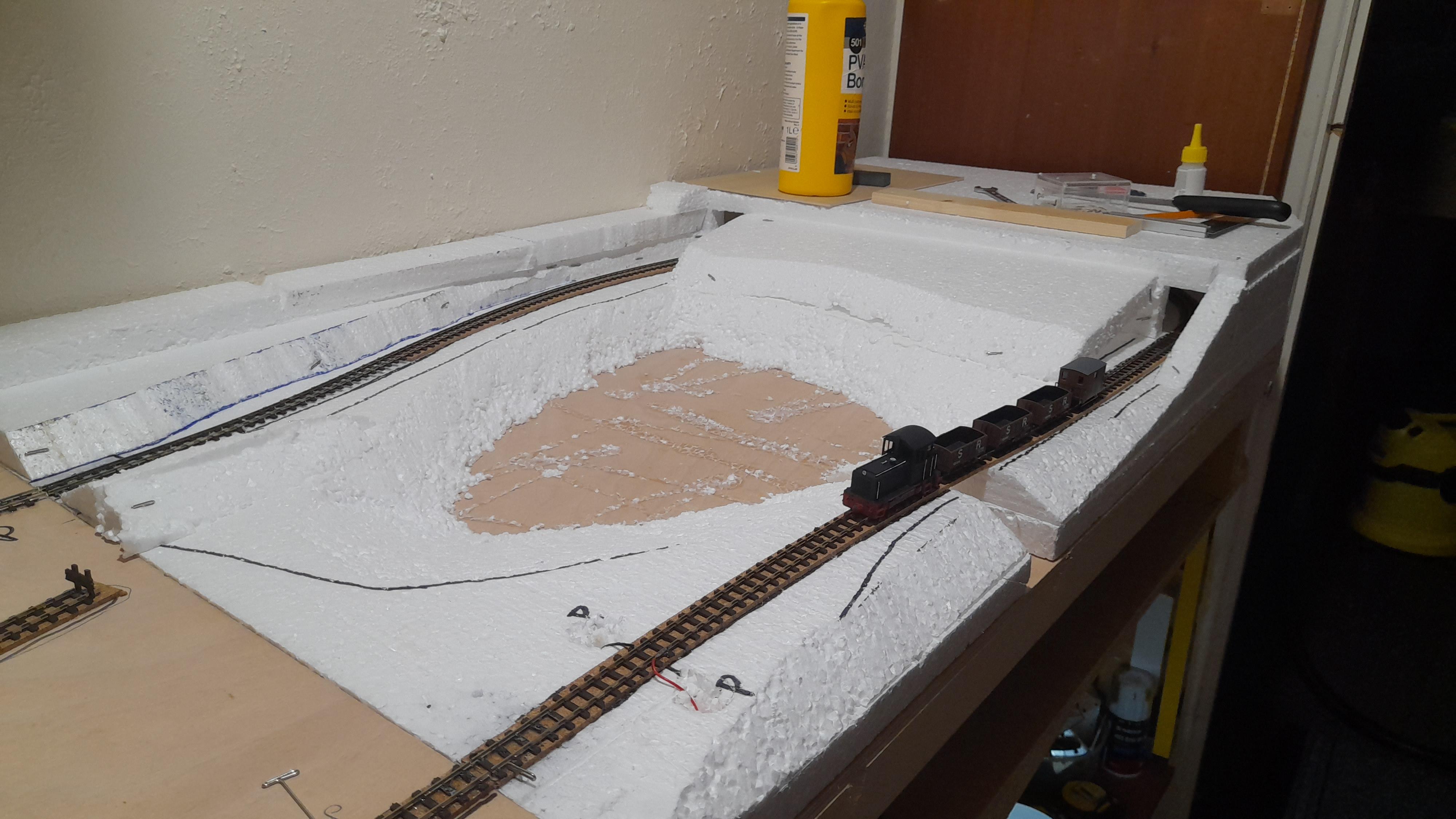 Hairy white bbw man posing nude in a workshop with a model train layout