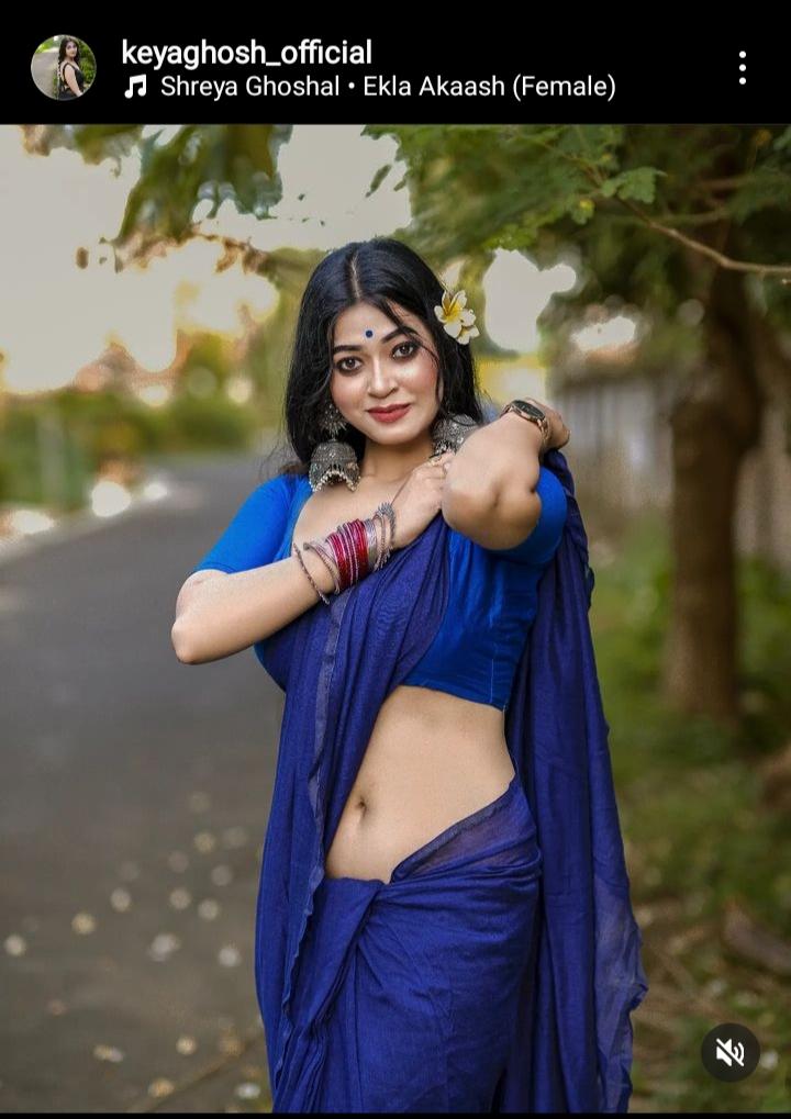 Keya Ghosh in a blue saree and blouse, showing her midriff and navel while posing outdoors.