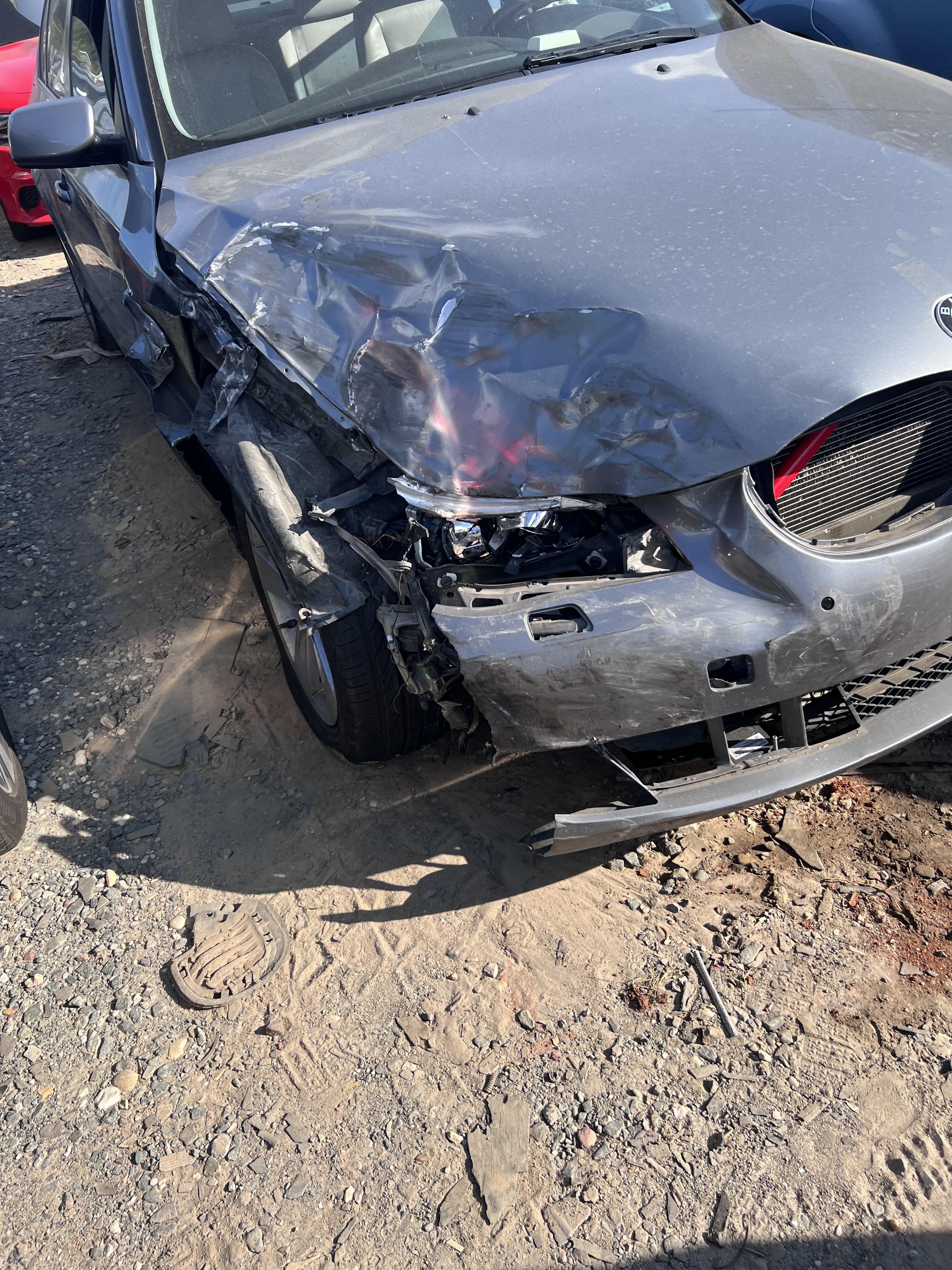 Close-up of a damaged grey BMW car with severe front-end passenger side impact in a dirt lot.