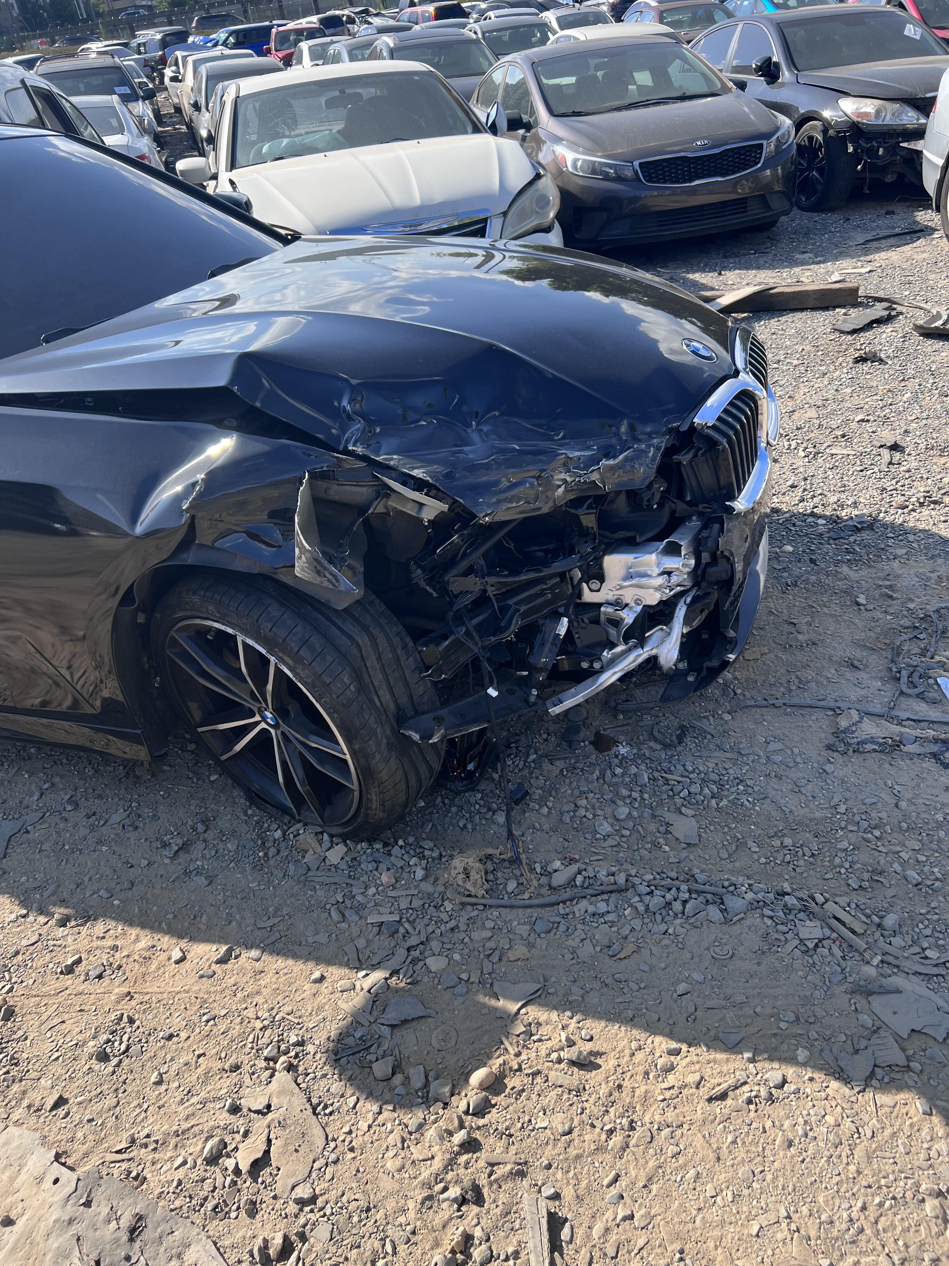 Close-up of a damaged grey BMW car with severe front-end passenger side impact in a dirt lot.